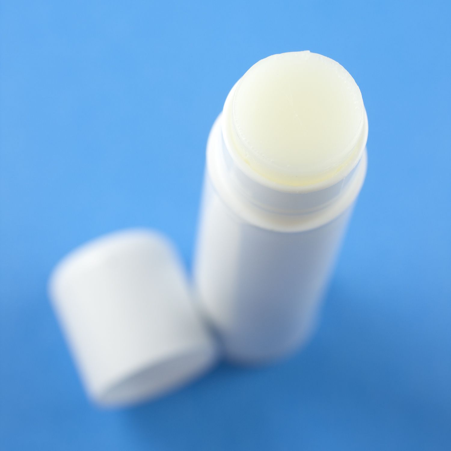 Top-view of an opened plain white chapstick, selective focus, on a blue background