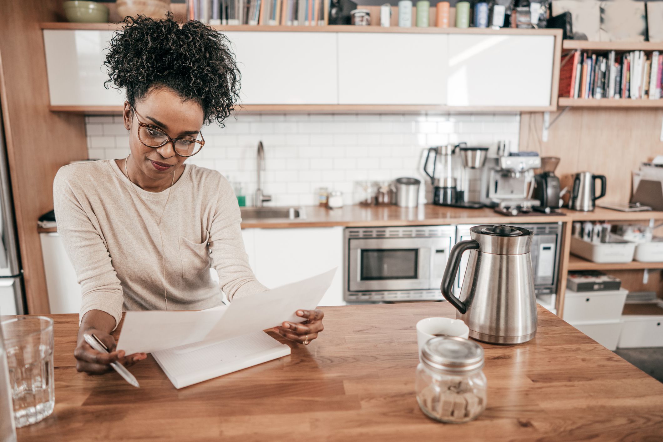 Woman sitting at her kitchen table, going over paperwork, with organized kitchen in the background