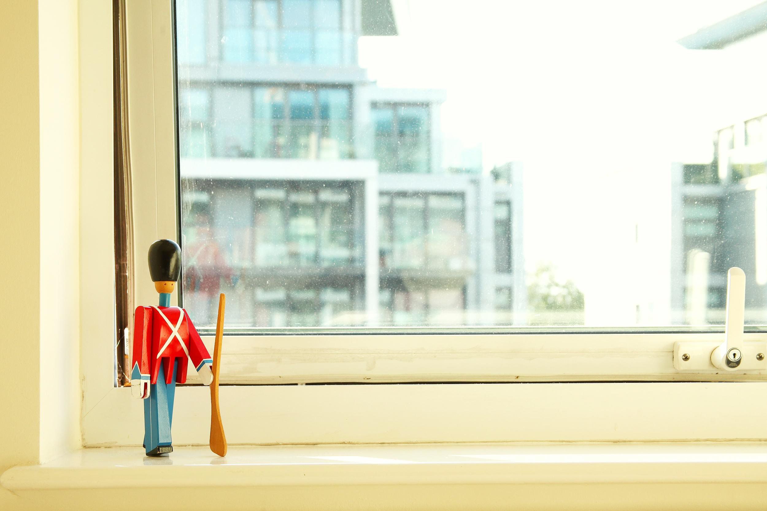 Wooden toy soldier on white window sill, closed window showing sun shining on building across the street