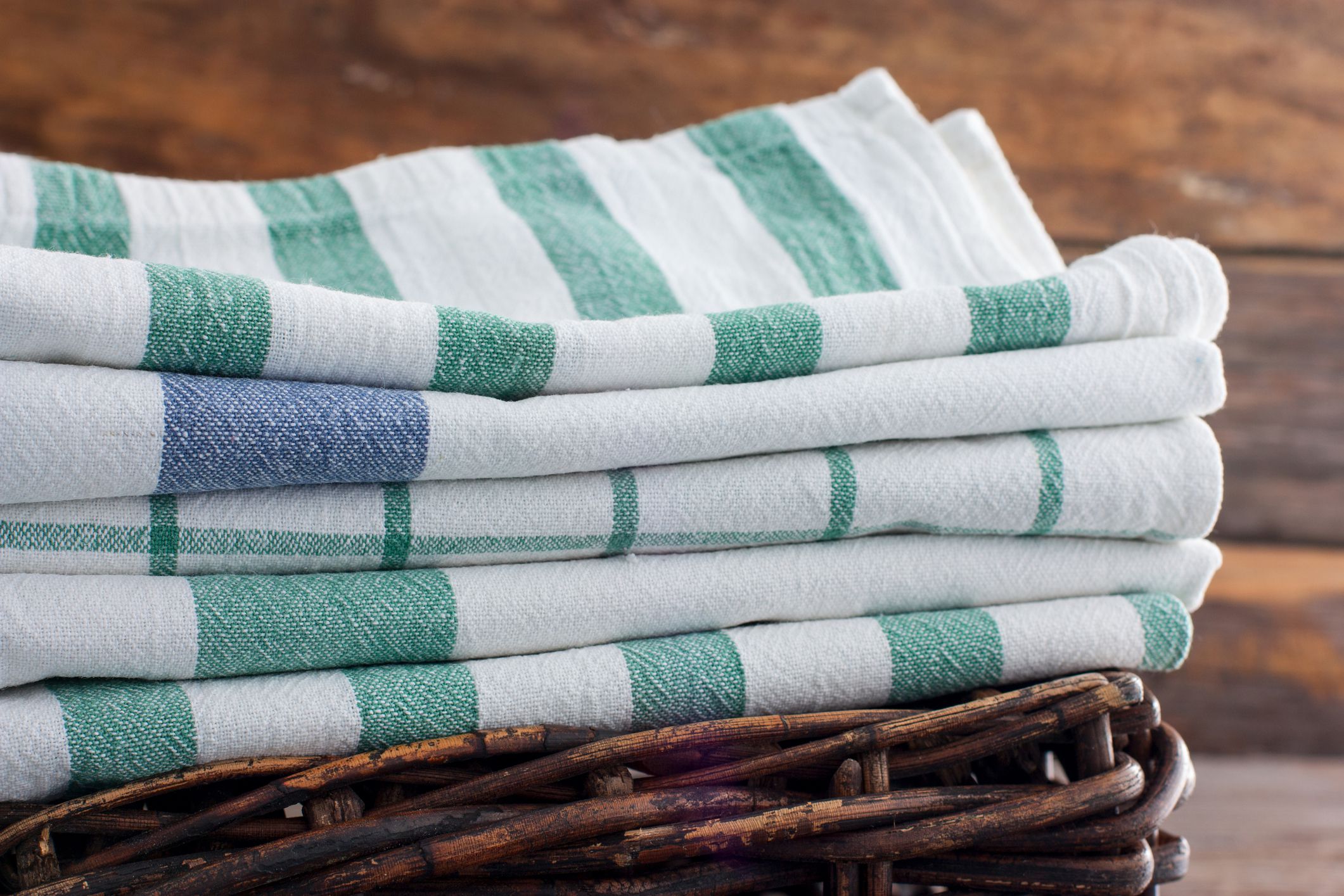 kitchen towels stacked in basket, wooden background