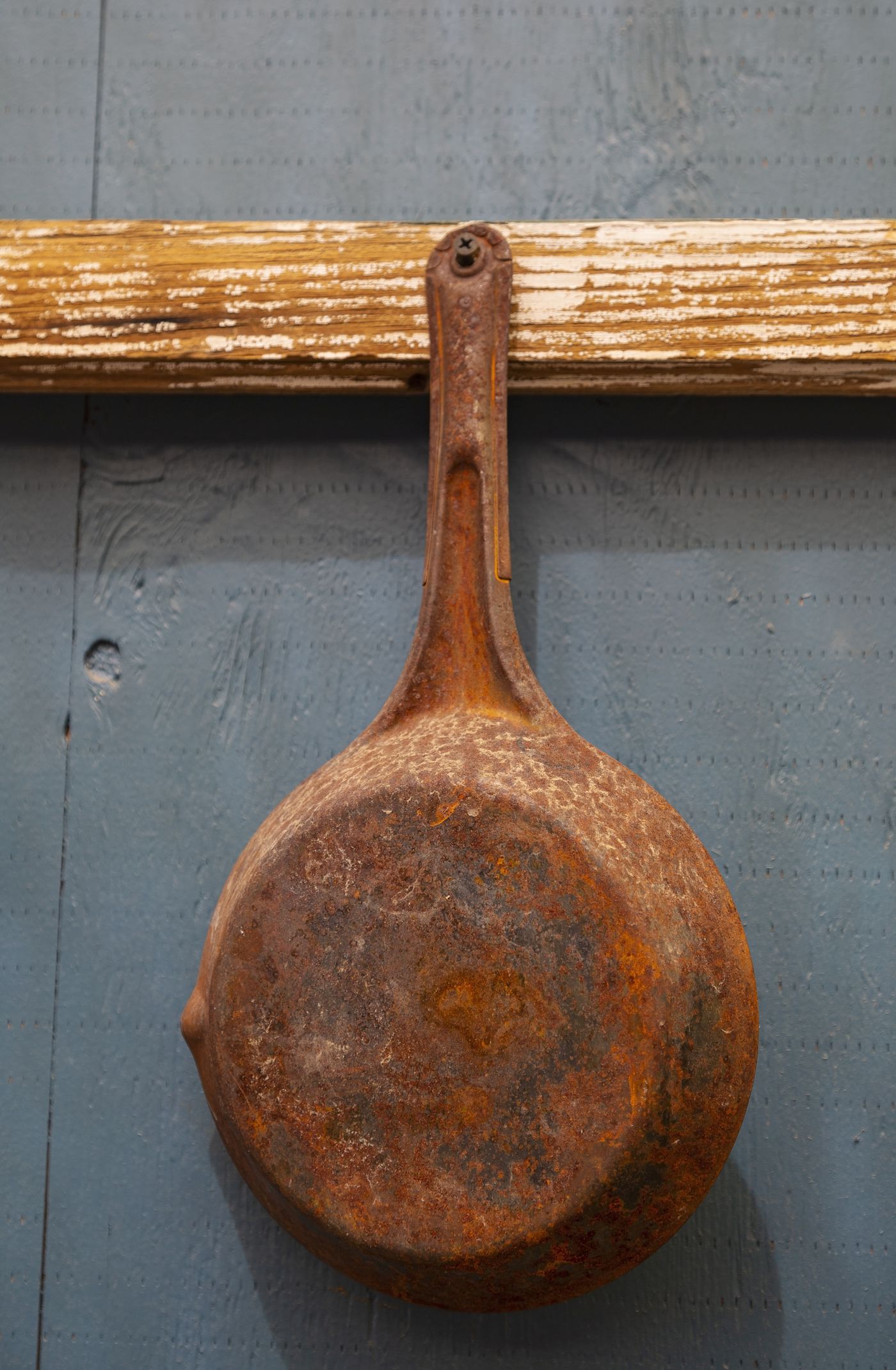 Old rusted cast iron frying pan hanging on wall