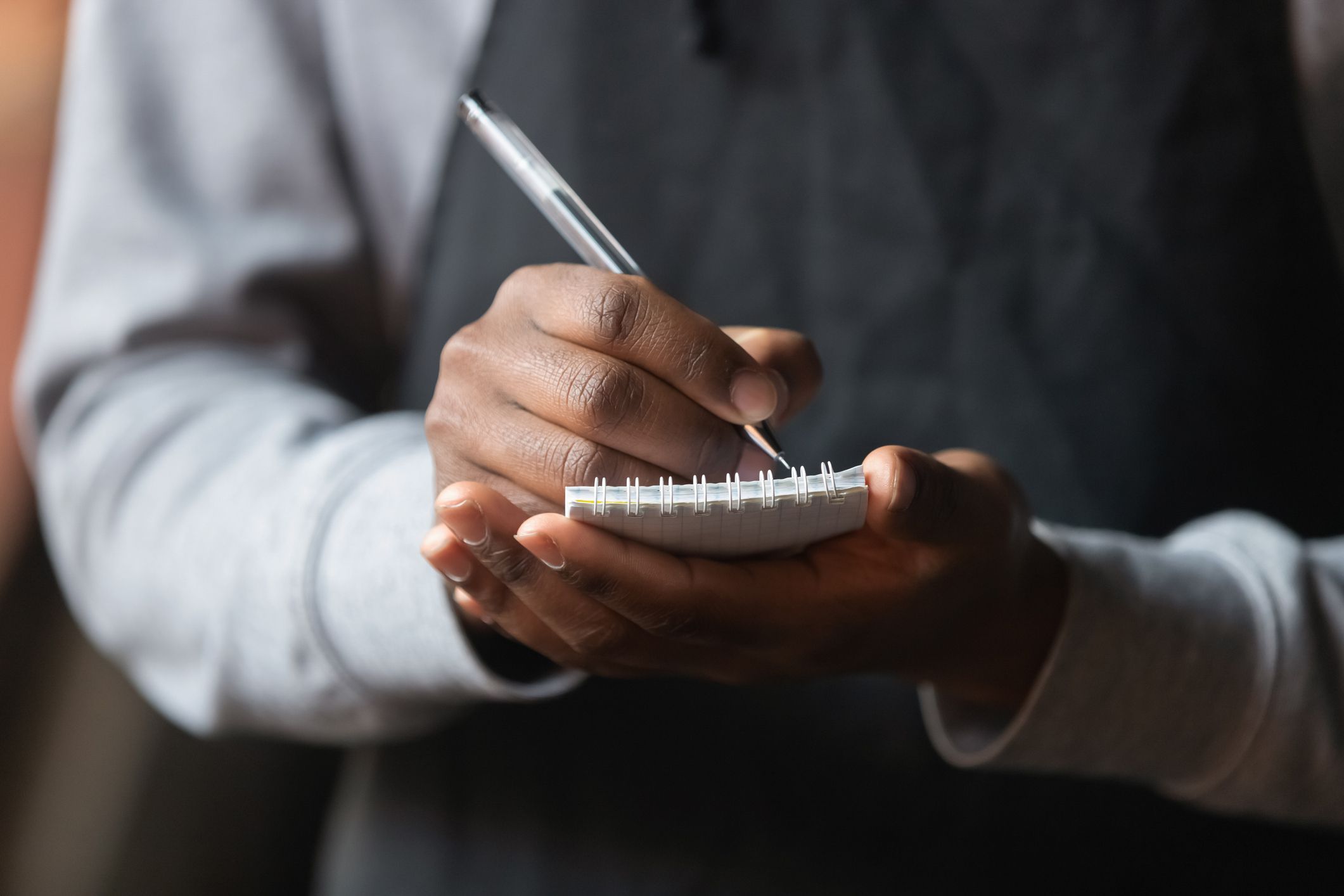 Close up African American waiter hands with notebook, taking customer order in cafe or restaurant, coffeehouse worker wearing black apron serving client, writing down, service concept