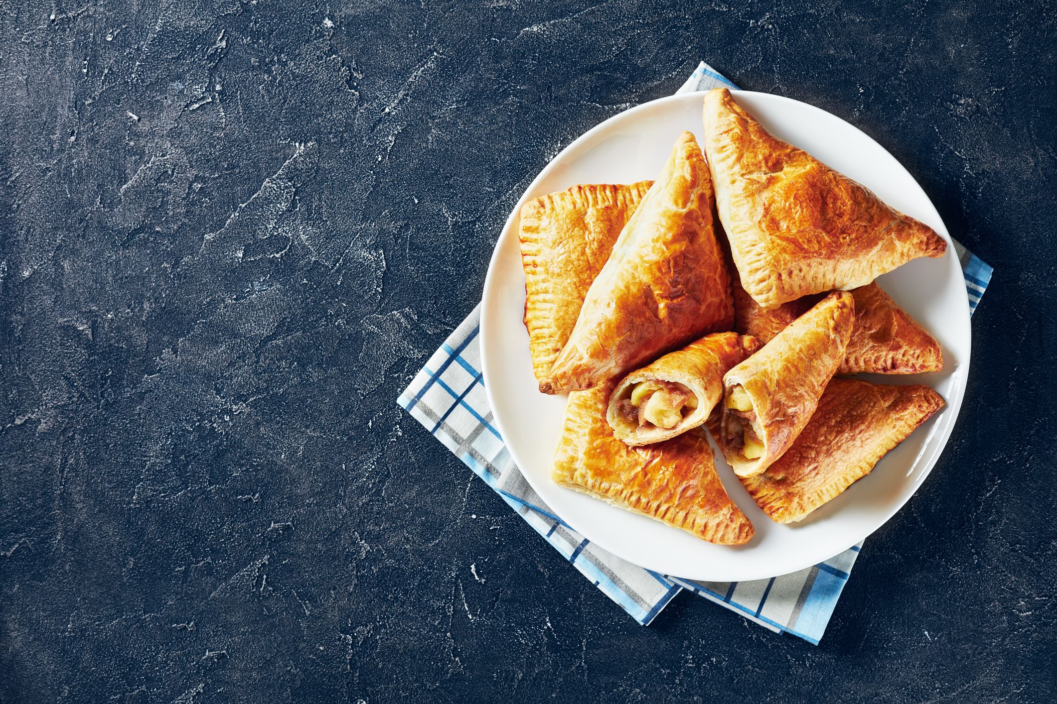 apple turnover on a white plate on a dark concrete table, horizontal view from above, flatlay, free space for text
