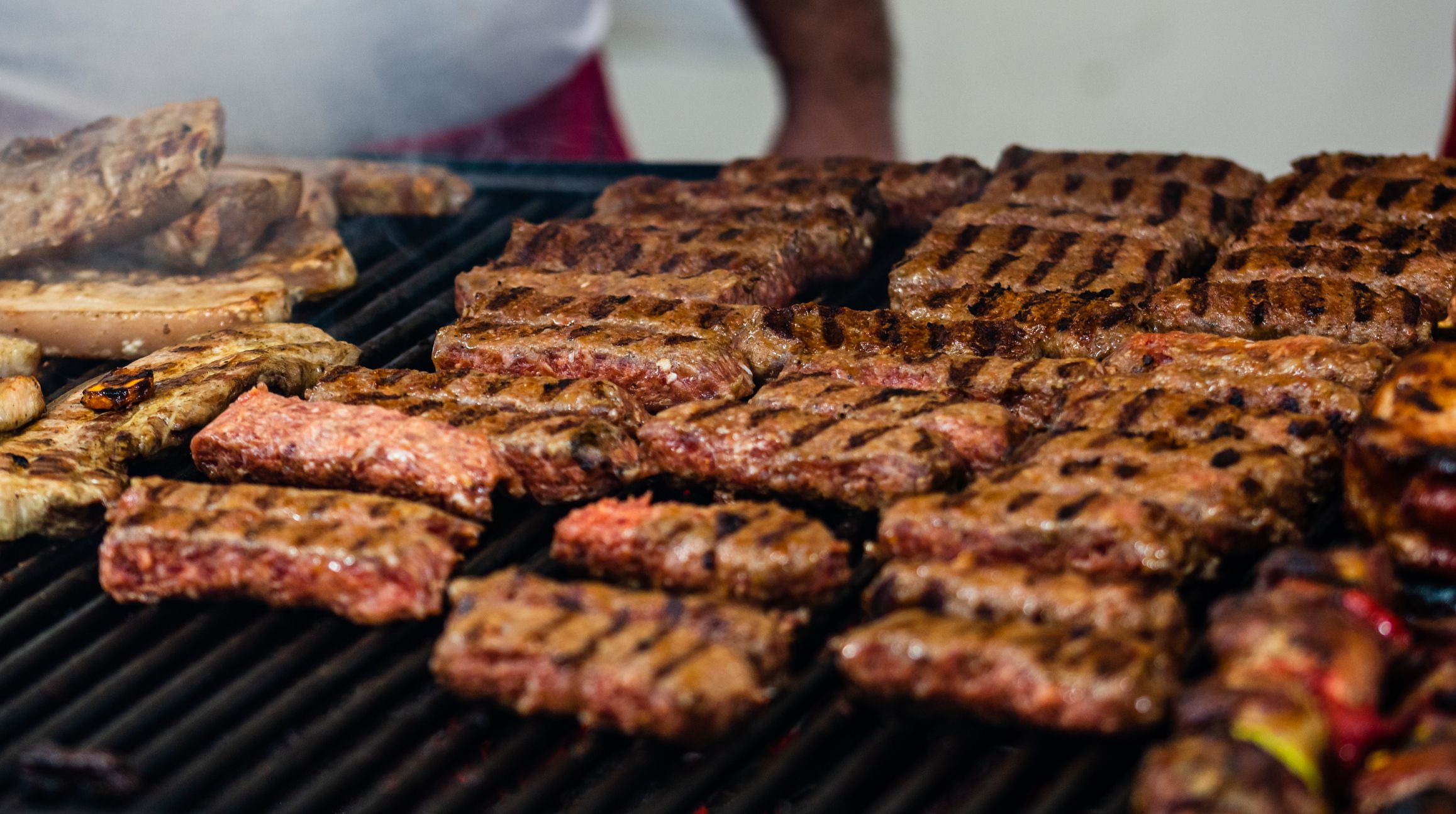 Juicy steaming meat on a charcoal grill, pork steaks, chicken breast, sausages, pieces of meat chops, Romanian minced meat (mici) at a street food festival
