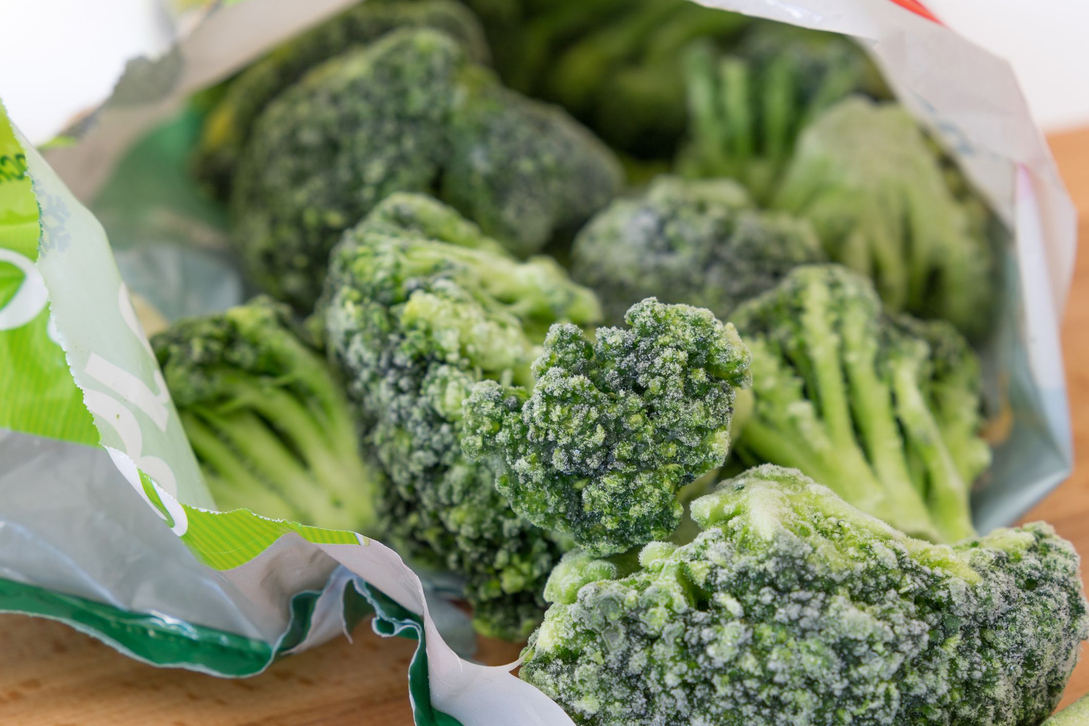 Close-up of frozen broccoli in an open bag on a wooden table