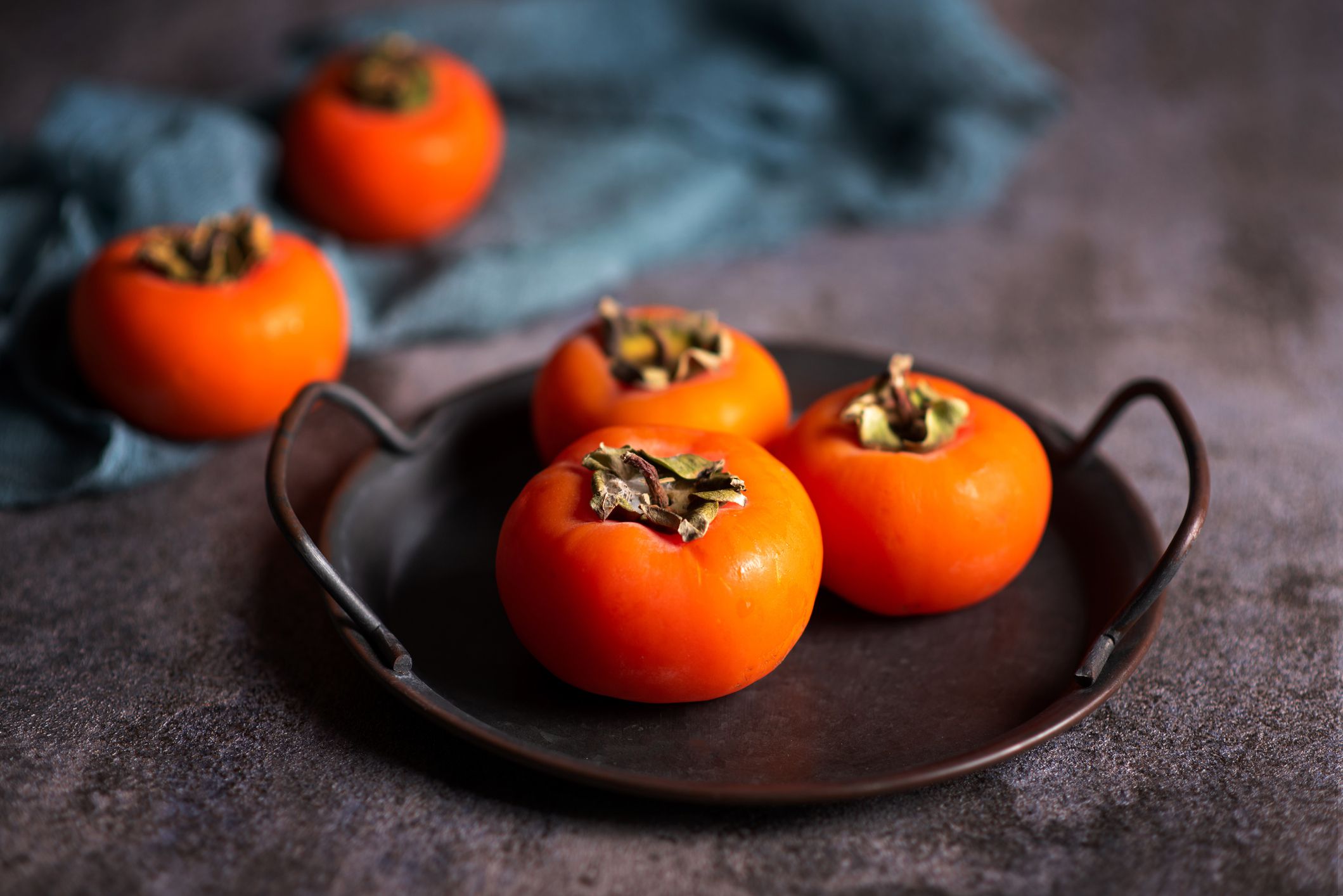 Persimmon orange kaki fruit on a artistic metal plate in a rustic dark setup