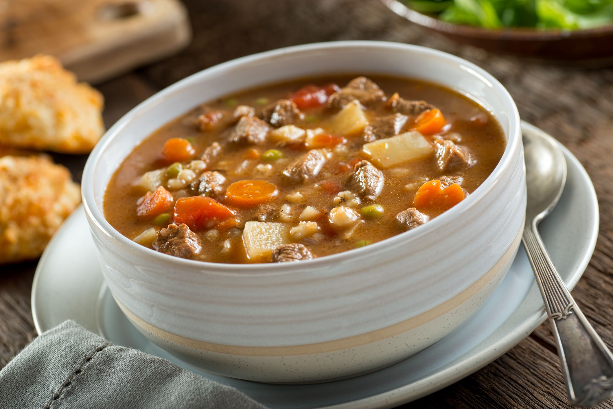 A bowl of delicious beef and barley soup with carrots, tomato, potato, celery, and peas.