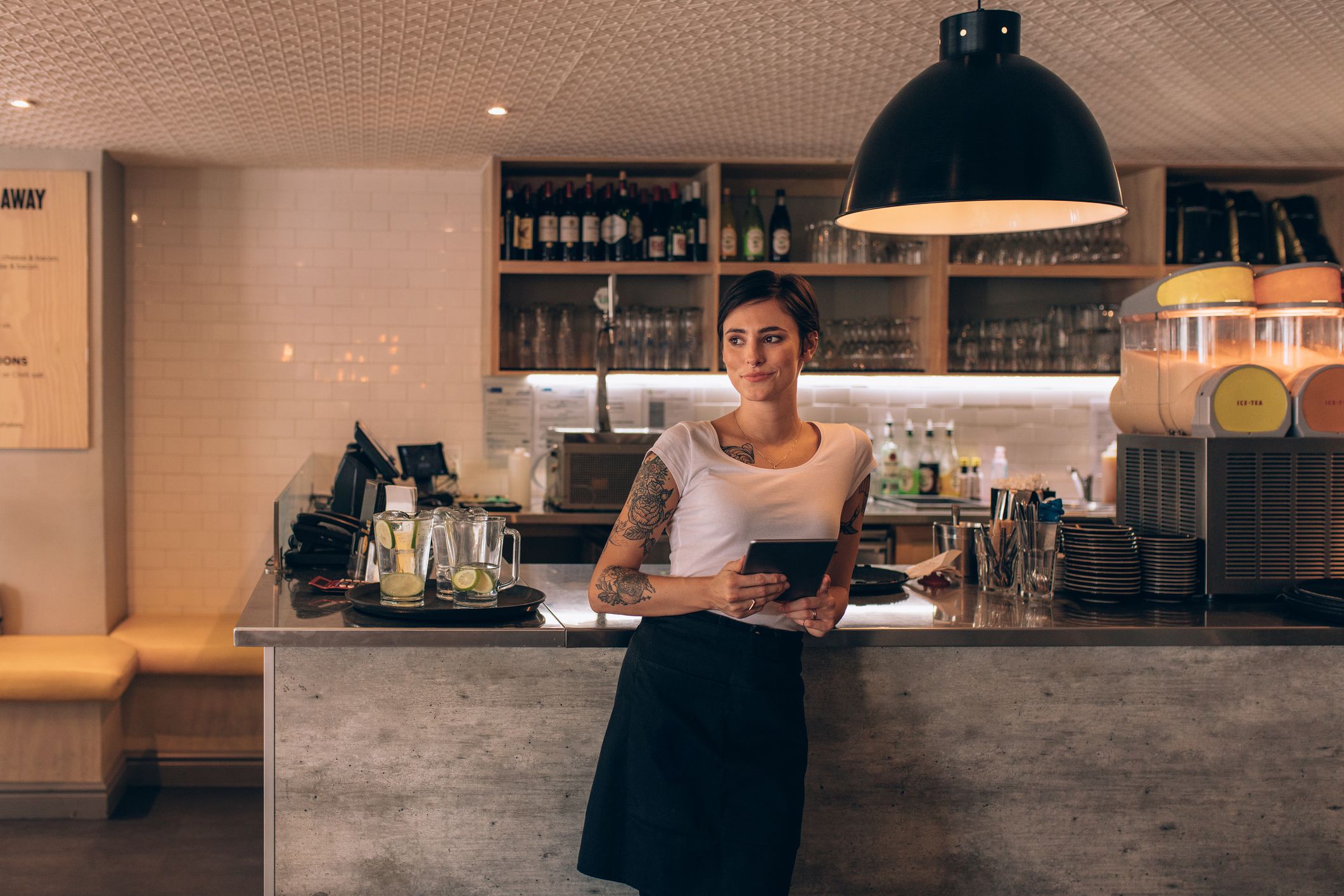 Portrait of beautiful young woman standing by coffee shop counter. Woman cafe owner standing with a digital tablet.