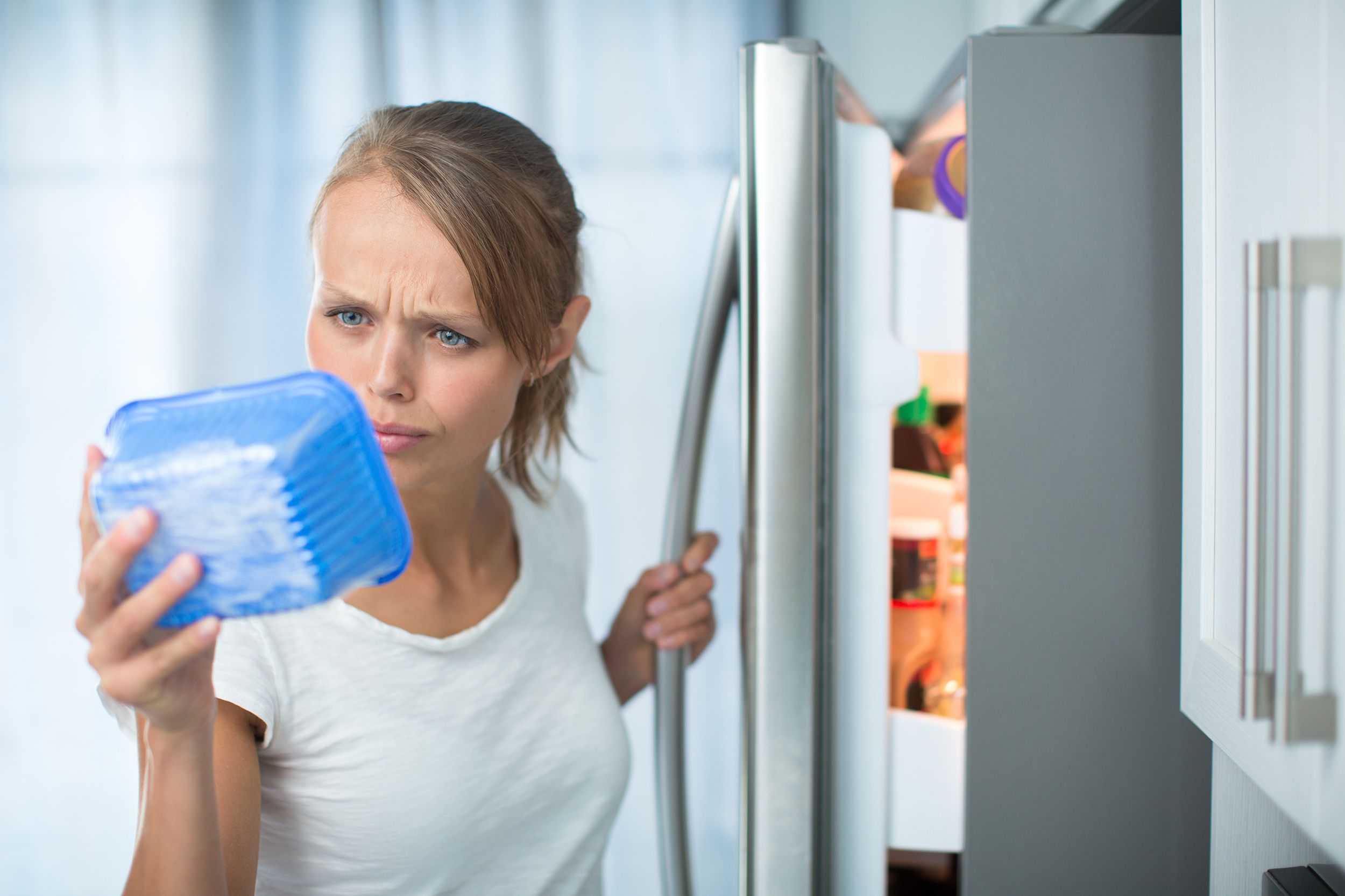 woman in her kitchen by the fridge, looking at the expiry date of a product she took from her fridge
