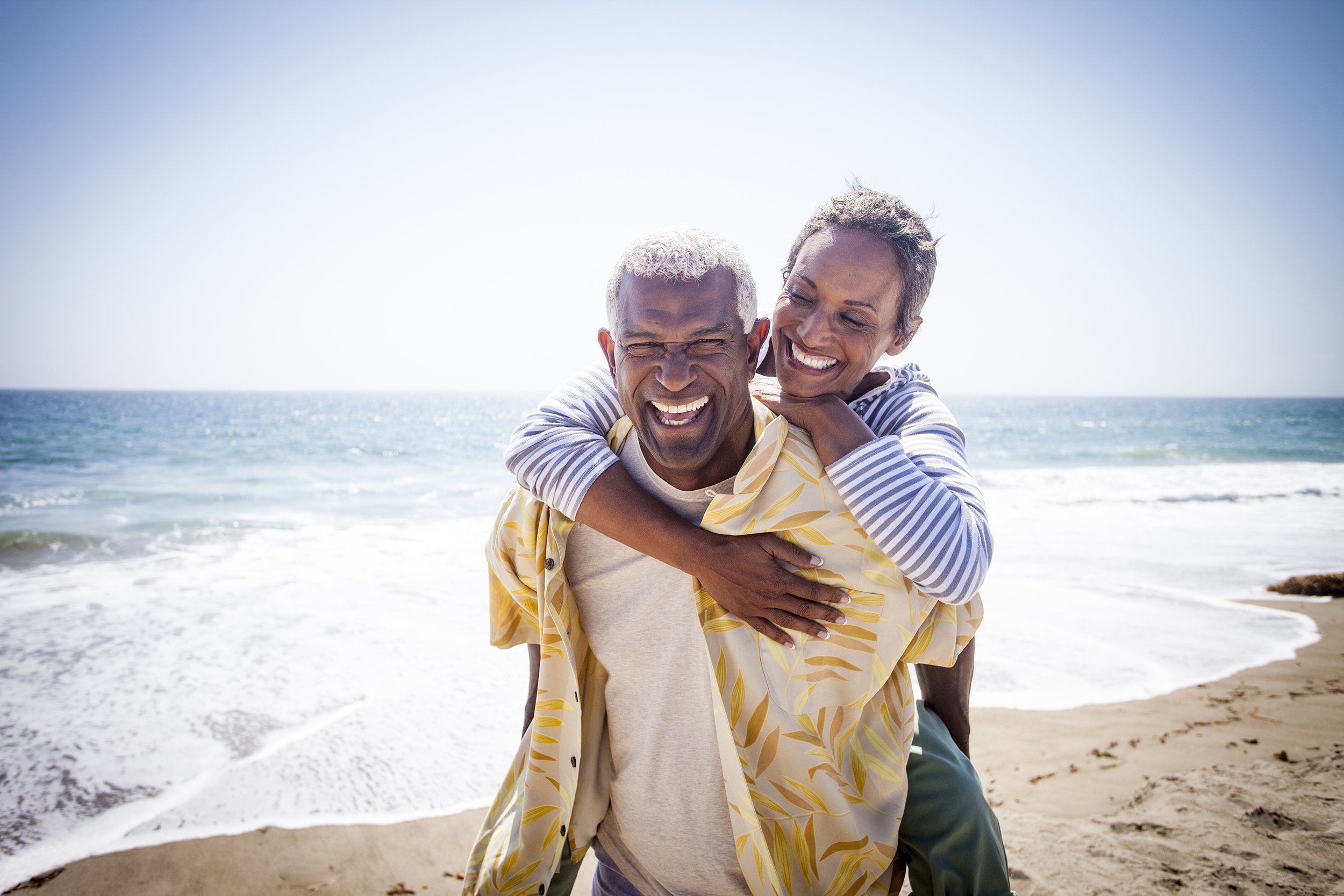 senior couple piggy backing on beach