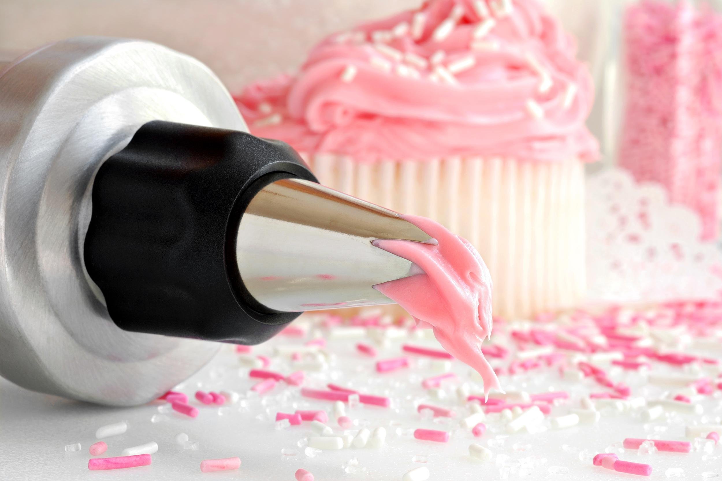 cake decorating fresh strawberry frosting dripping from pastry tip and cupcakes with sprinkles