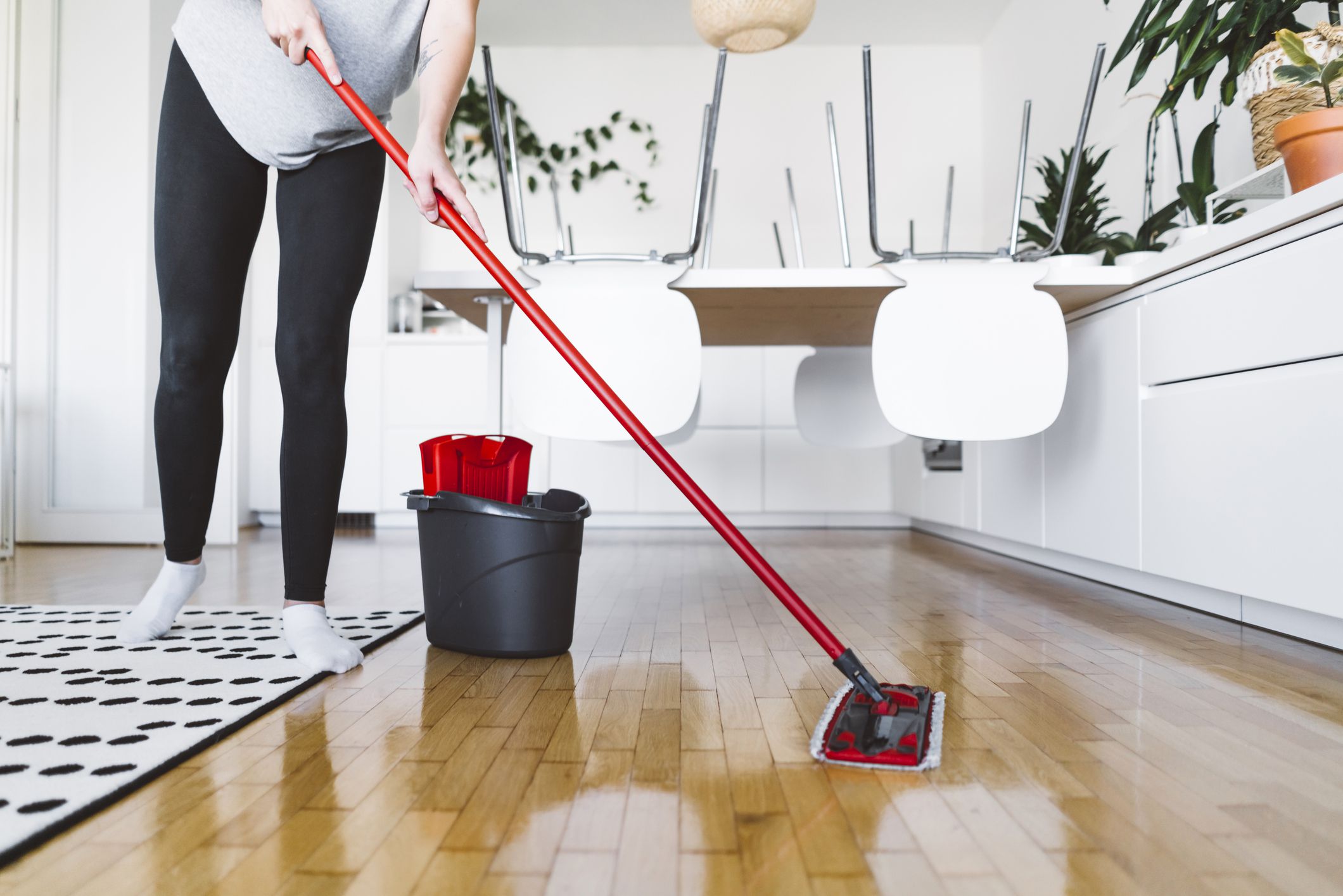 Unrecognizable woman cleaning the wood floors in her apartment using a red mop. Woman doing house chores, keeping her home nice and clean.