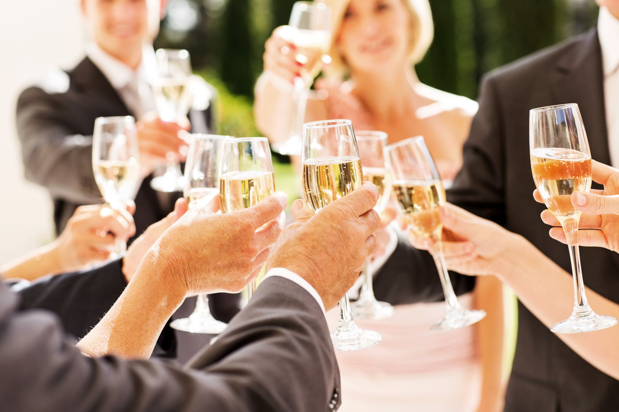 Midsection of guests and couple toasting champagne flutes at reception. Horizontal shot.