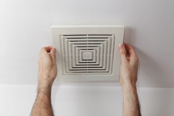 A person&rsquo;s hands are removing or installing a white ceiling air vent cover against a white ceiling.
