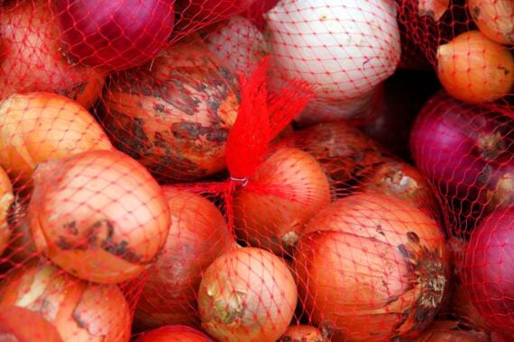 A close-up of yellow and red onions packed inside a red mesh netting.
