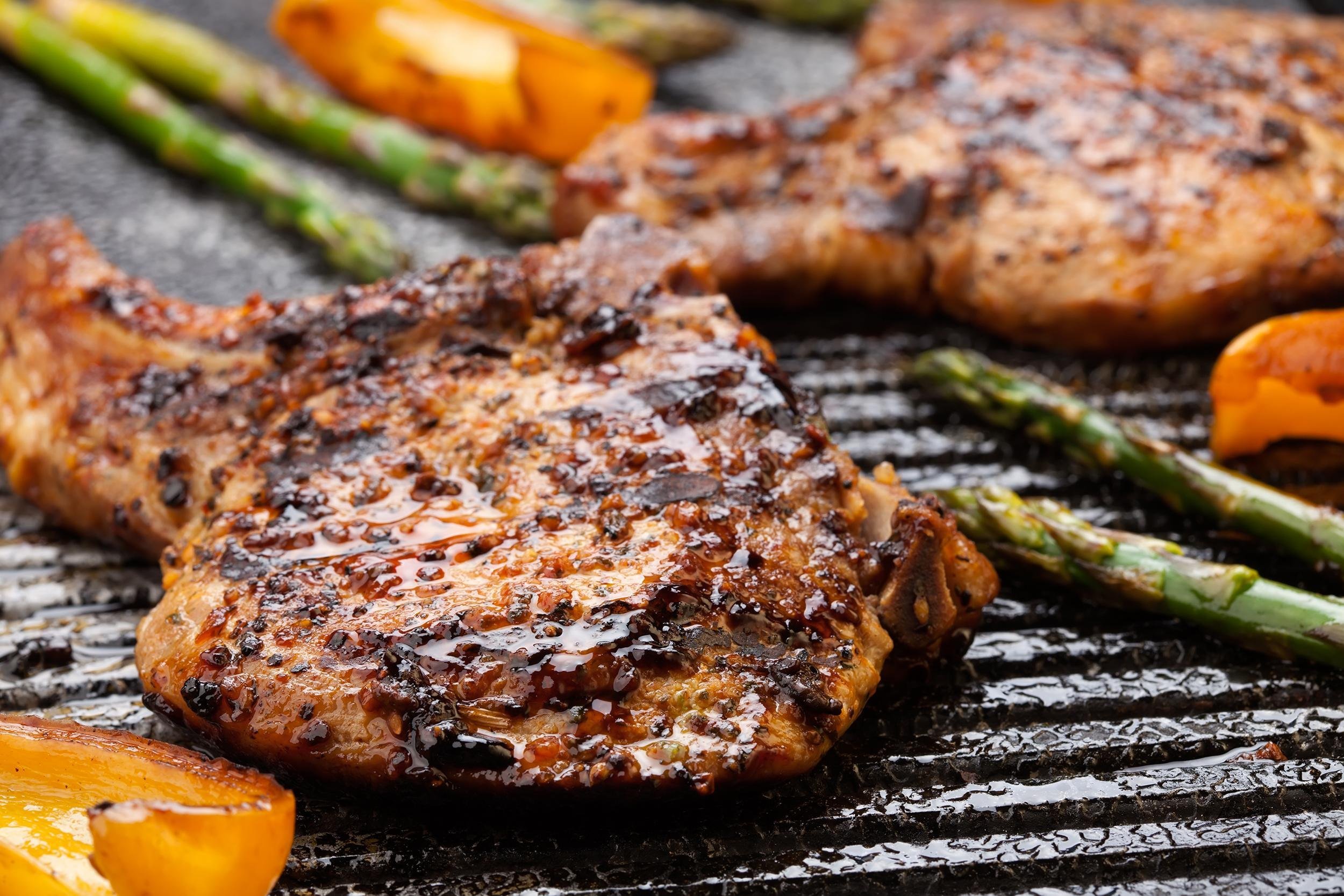 pork chops are grilled on griddle with asparagus and bell pepper