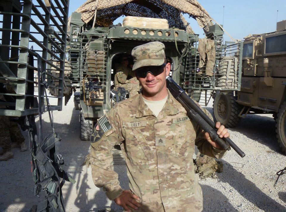 Sgt. Joseph M. Lilly stands in his US Army uniform surrounded by military vehicles and other Army gear