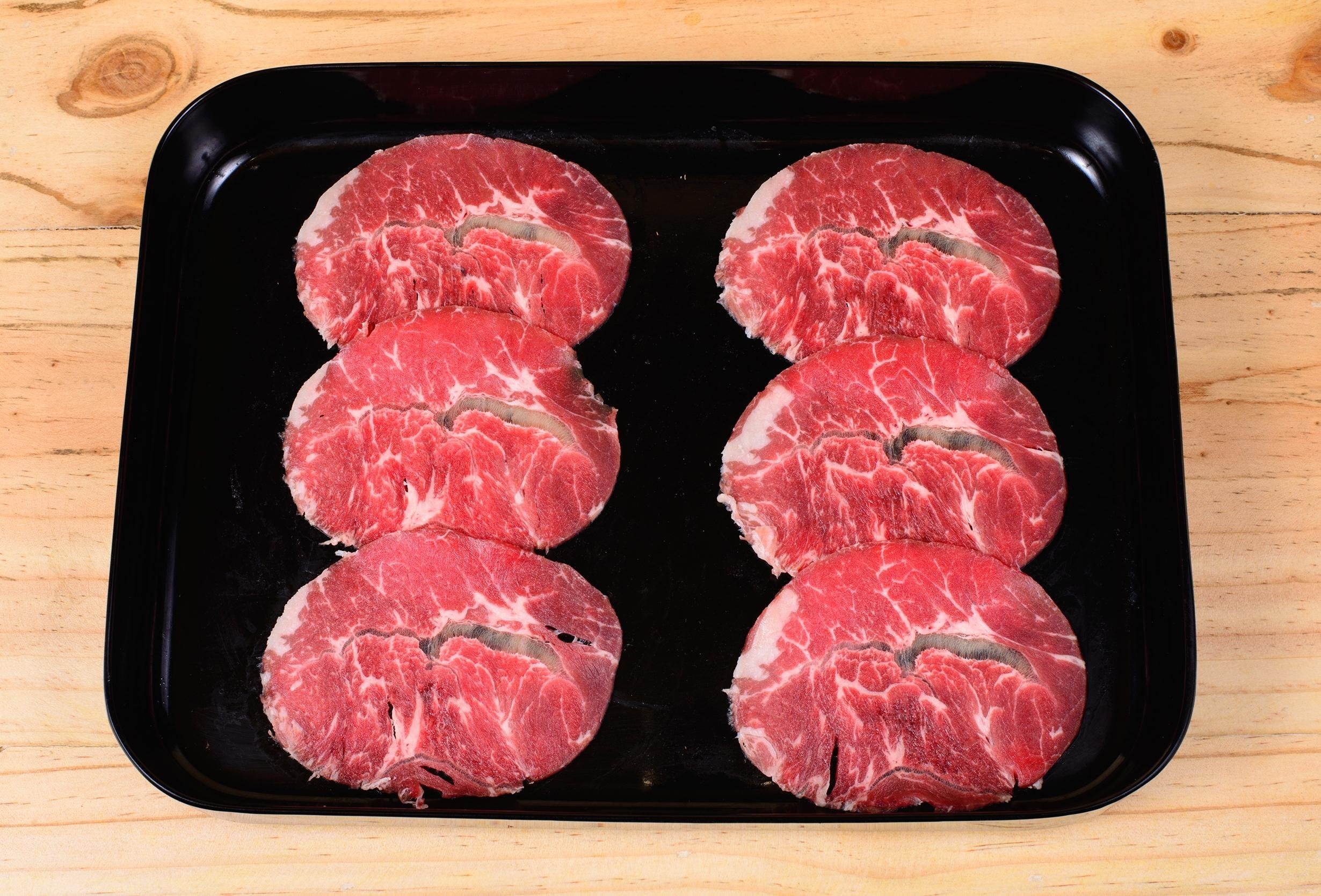 raw beef chuck eye in black tray on wood table