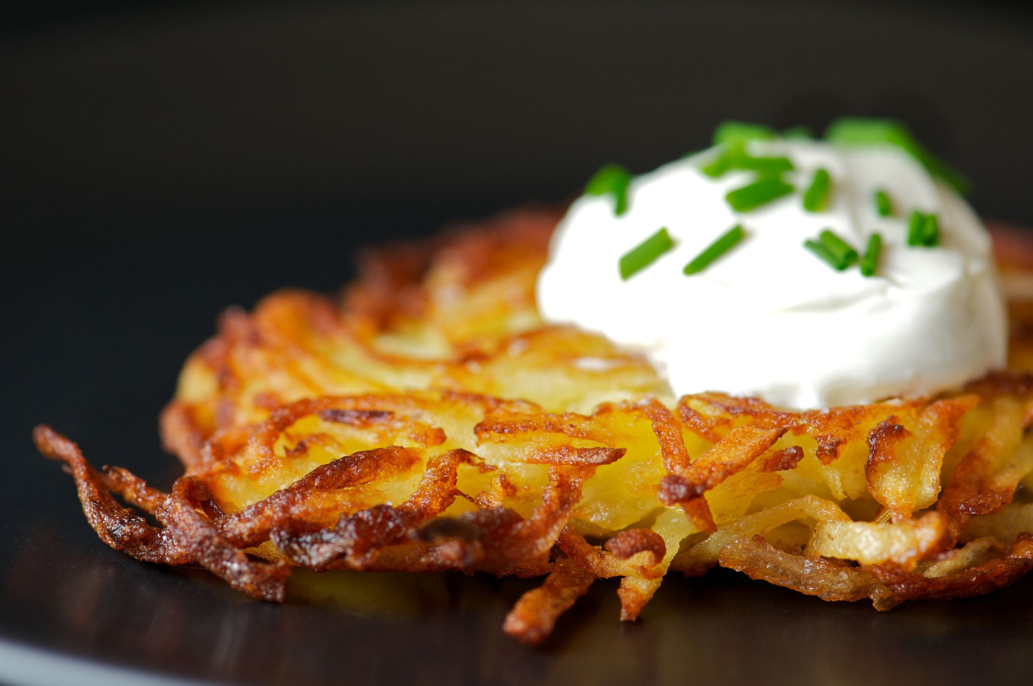 A Latke With a Dollop of Sour Cream on a Black Plate, Selective Focus