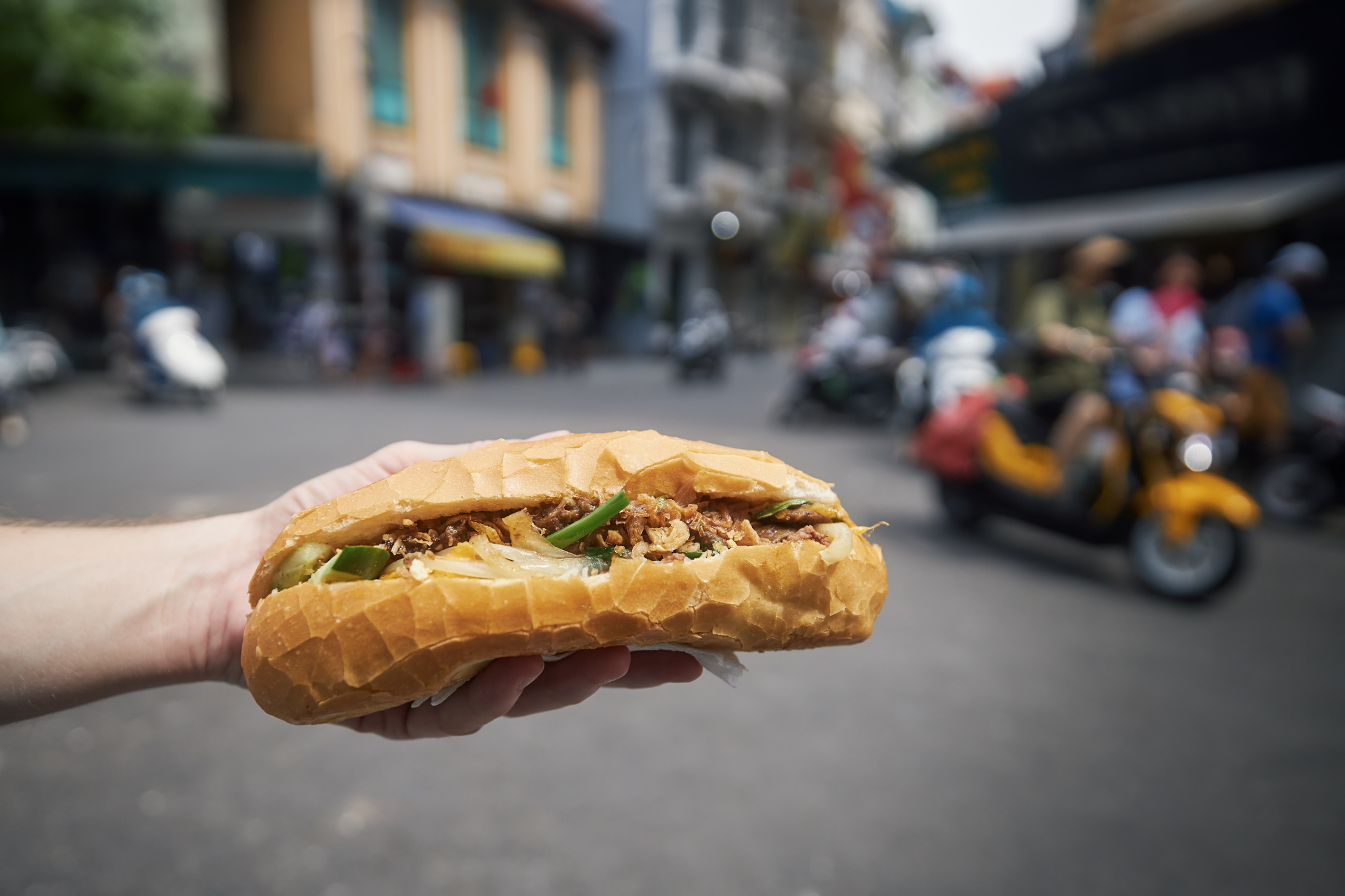 Hand Holding a Bánh Mi With Street in Hanoi, Vietnam in the Background