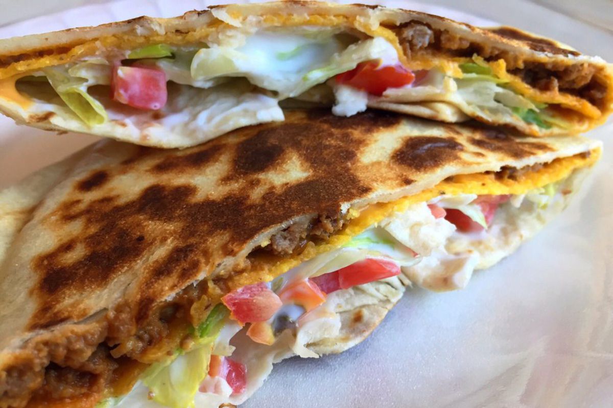 Closeup of Taco Bell Crunchwrap Supreme, one slice on top of the other, on a white paper plate