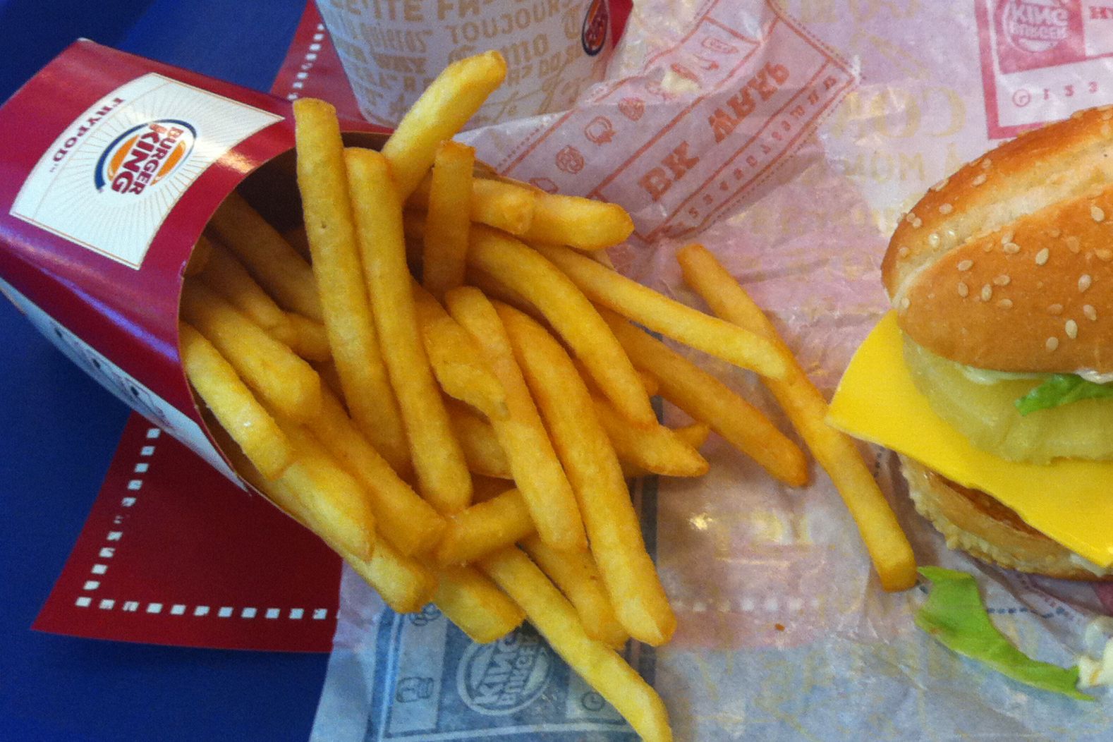 Focus on Burger King large fries on serving paper, a Whopper Jr. on the right side, on a red paper, on a blue table
