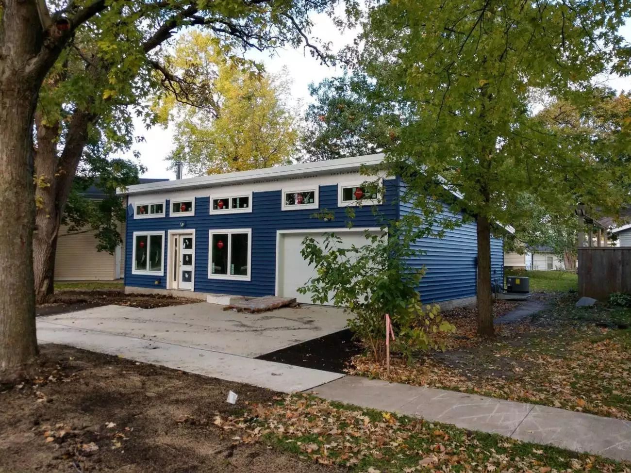 Front exterior of Mighty Small Homes Modern, blue paint with white accents, concrete patio with walkway, surrounded by trees in a yard