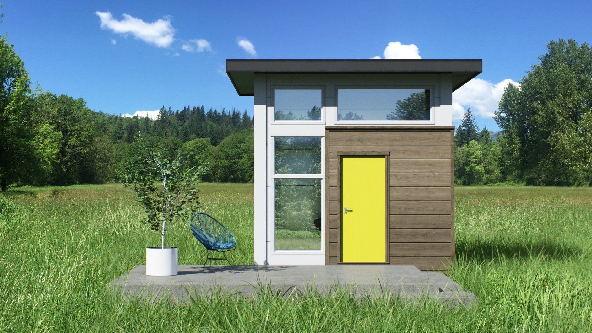 Front exterior of NOMAD Cube, many windows, wooden front area with a bright yellow door with a concrete front porch, on a grassy lawn with trees in the background on a sunny day