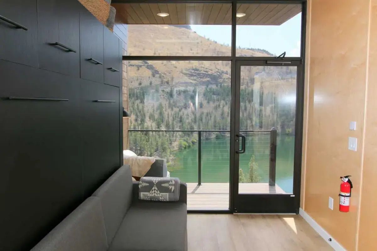 Interior of Tiny Heirloom eXpanse, left side is black cabinets, right side is a wooden wall, mountains and lake seen through the large window