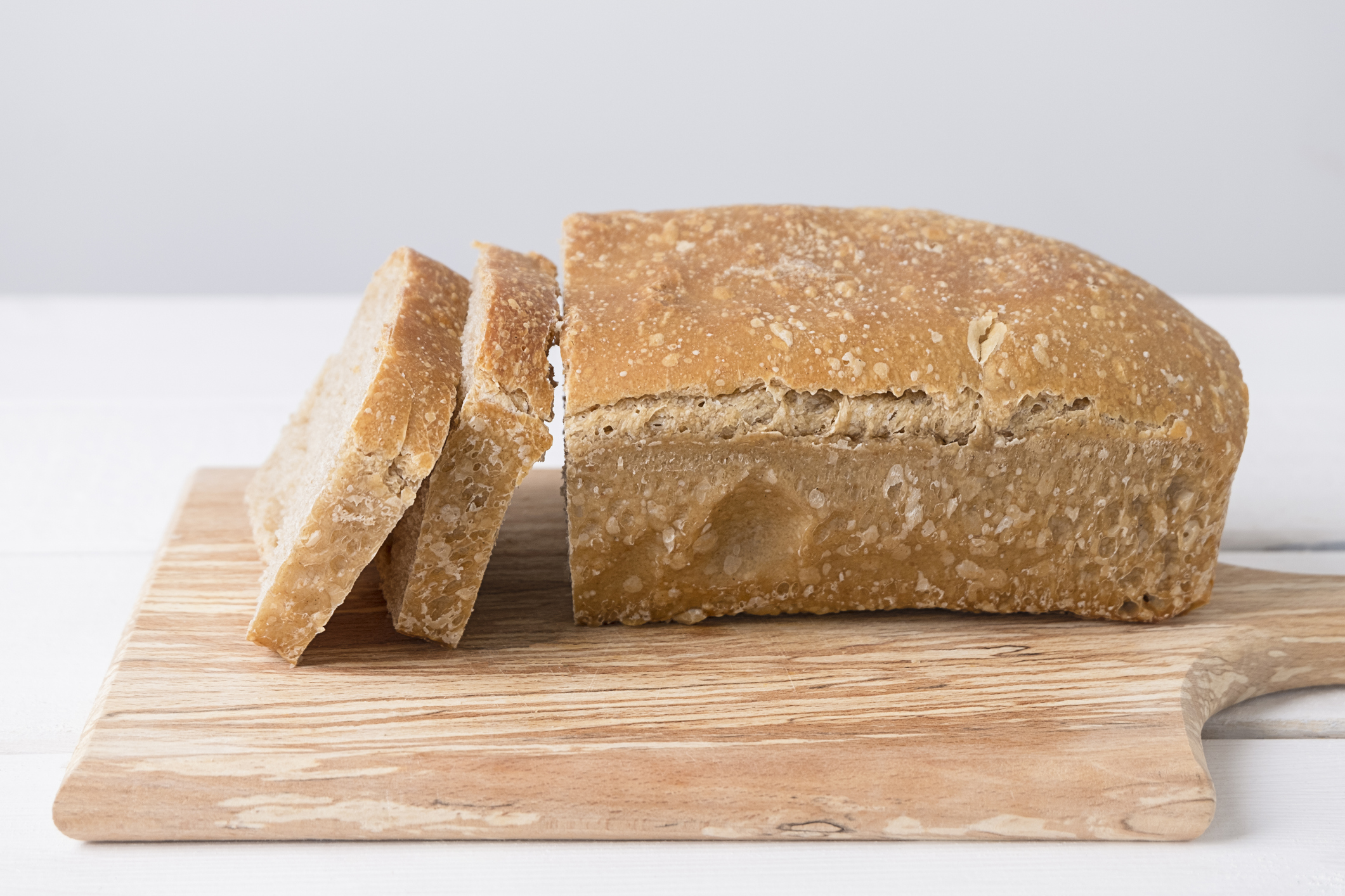 Loaf of White Sourdough Bread With a Few Pieces Cut, on a Wooden Cutting Board