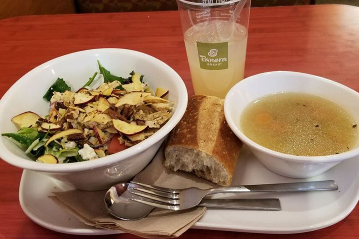 Panera salad and homestyle chicken noodle soup with bread and lemonade on a white serving tray with utensils and napkins on a wooden table at Panera