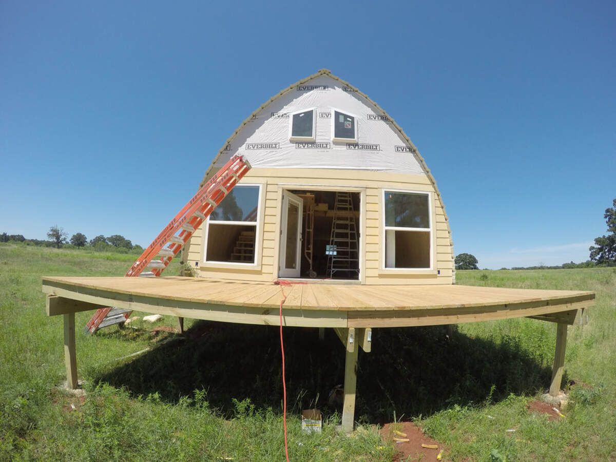 Front exterior of Texas Arched Cabins 24-by-40-Feet Wide Arched Cabin in the process of being built, large elevated porch in the foreground, on a large country lot on a sunny day