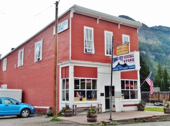 The historic red Cooke City General Store building with signage and an American flag.