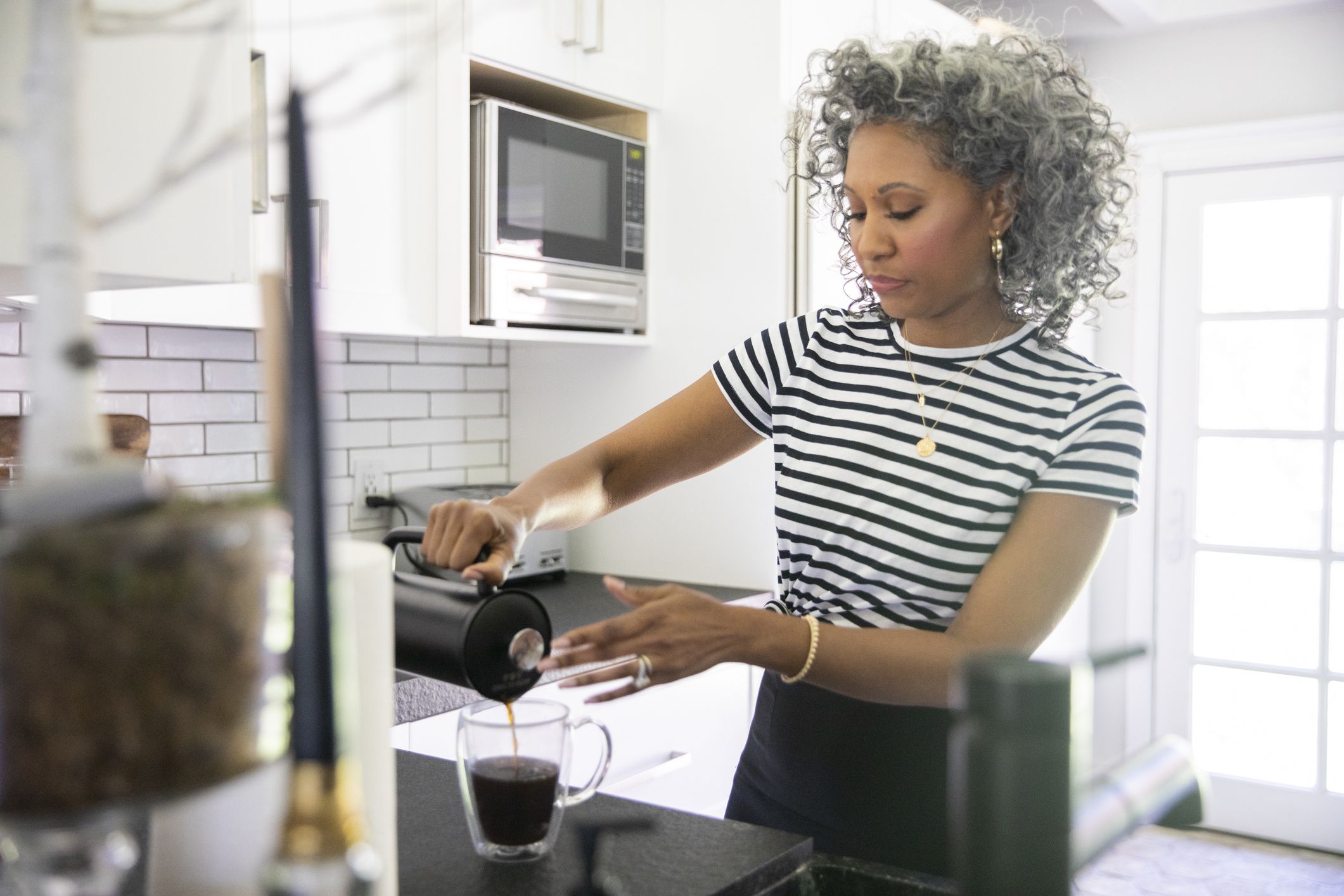 A beautiful black woman with white curly hair makes coffee.