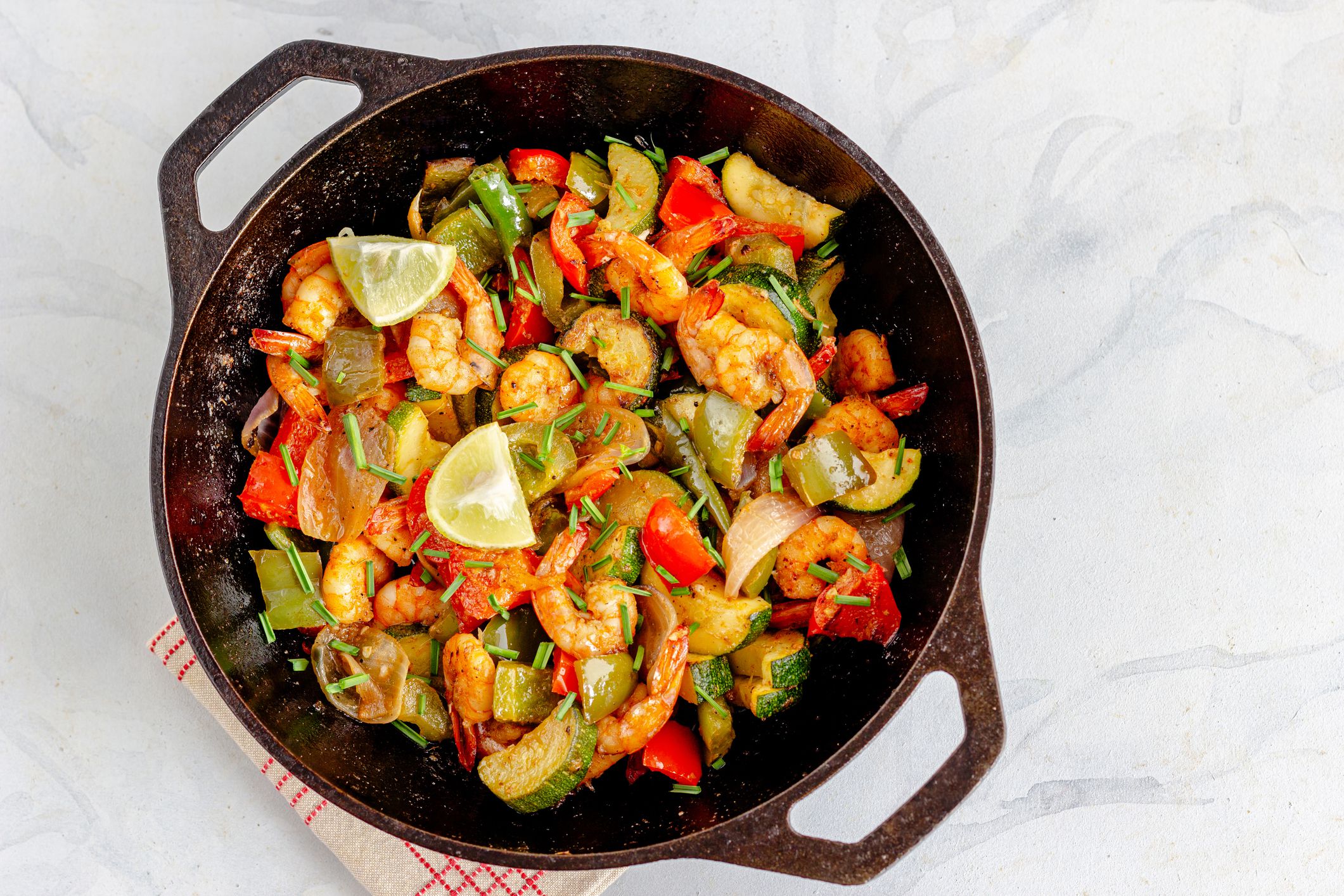 Stir-Fried Shrimp with Vegetables in a Cast Iron Wok Garnished with Garlic Chives and Lemon Top Down Photo