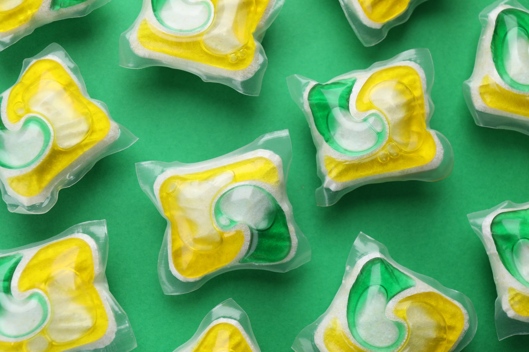 Many dishwasher detergent pods on green background, flat lay