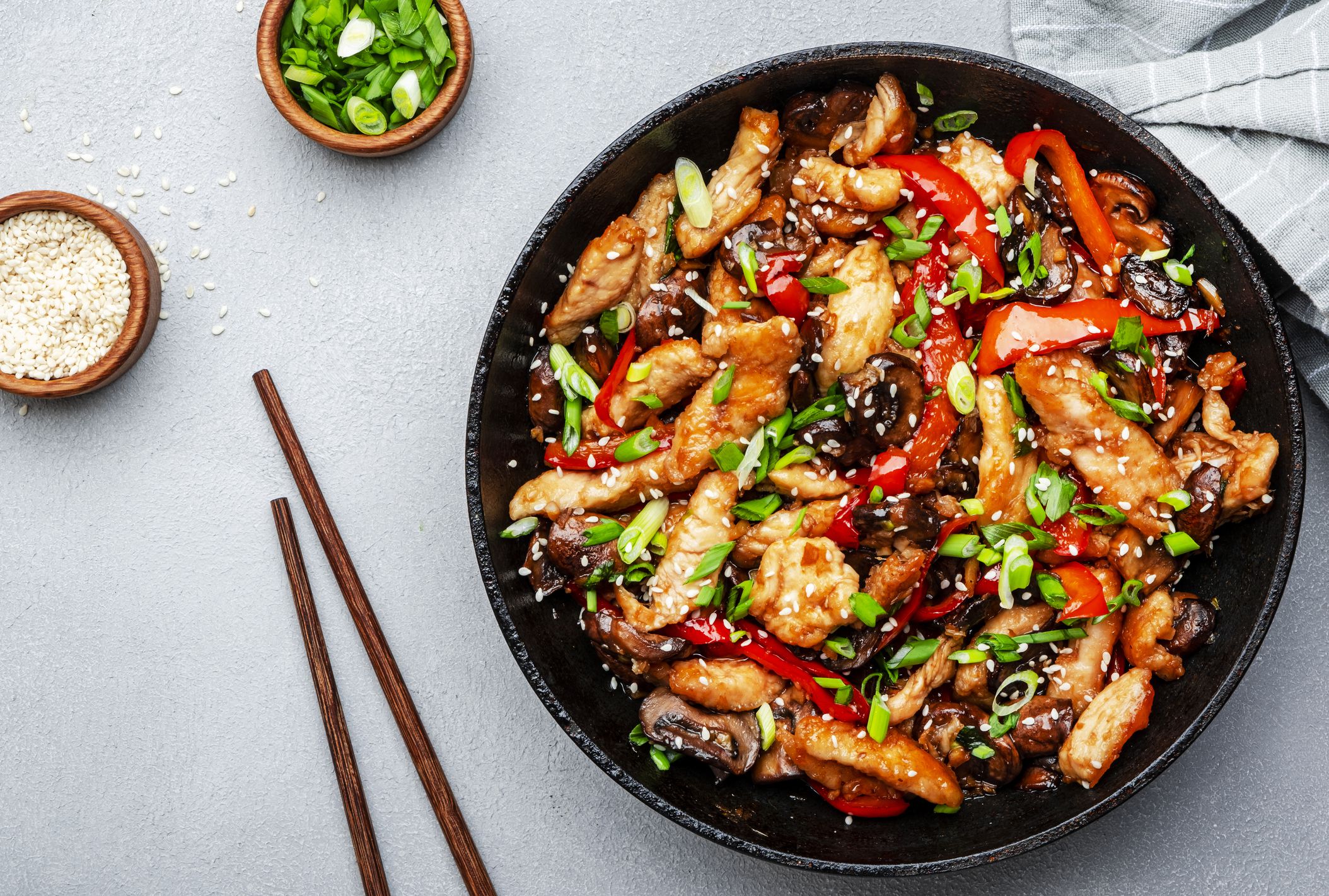 Stir fry with chicken, red paprika, mushrooms and chives in frying pan. Asian cuisine dish. Gray kitchen table background, top view, copy space
