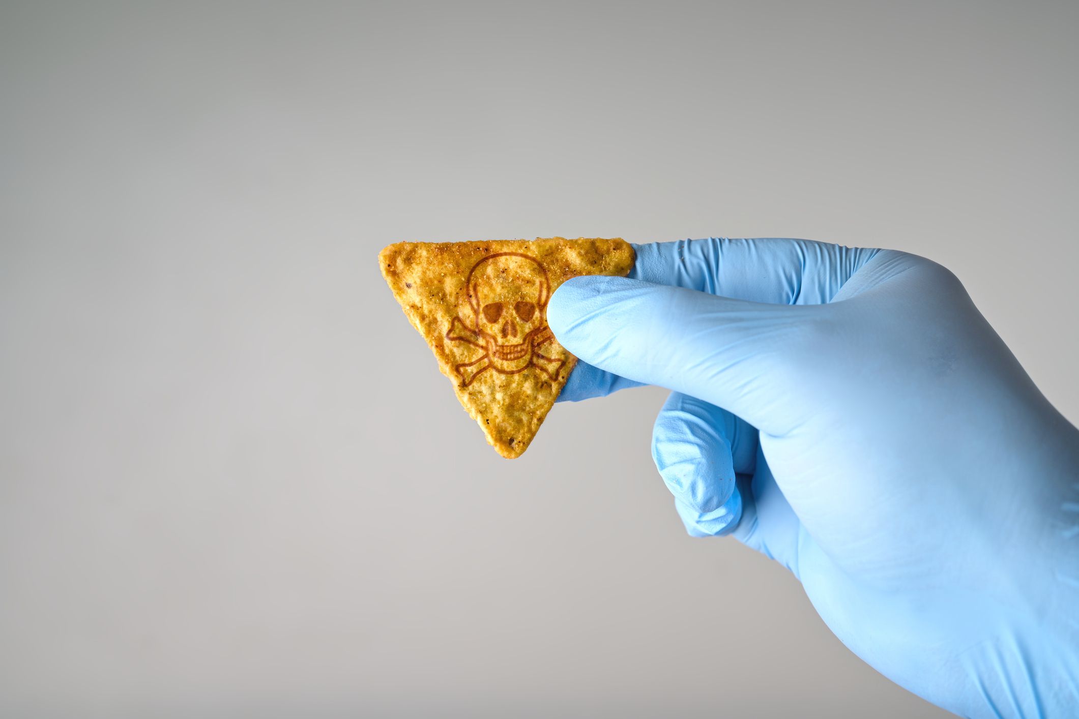 Gloved hand holding a hot tortilla chip with poison symbol. Concept for hot chip challenge.