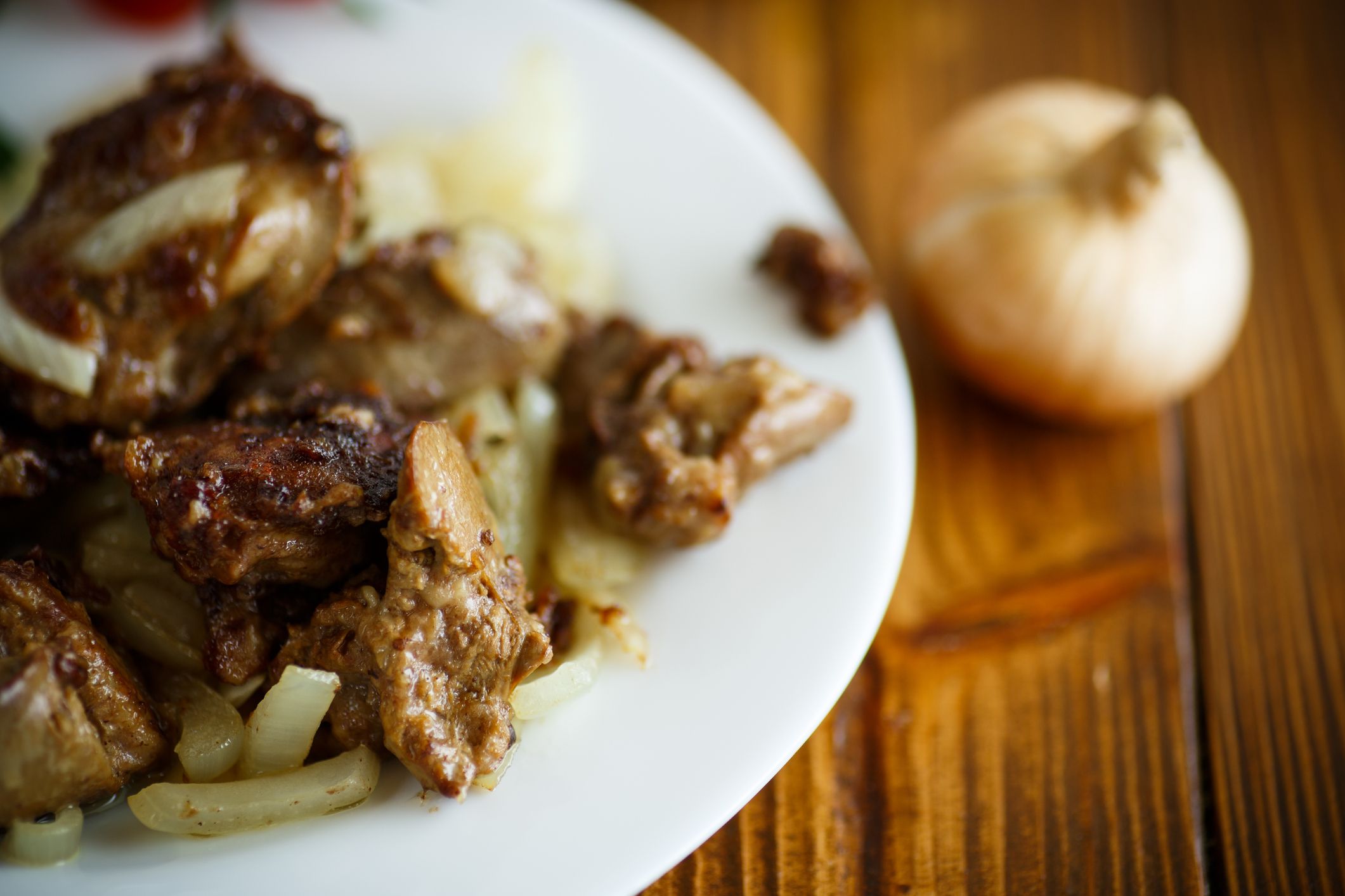 Fried chicken liver with onions on a plate with tomatoes