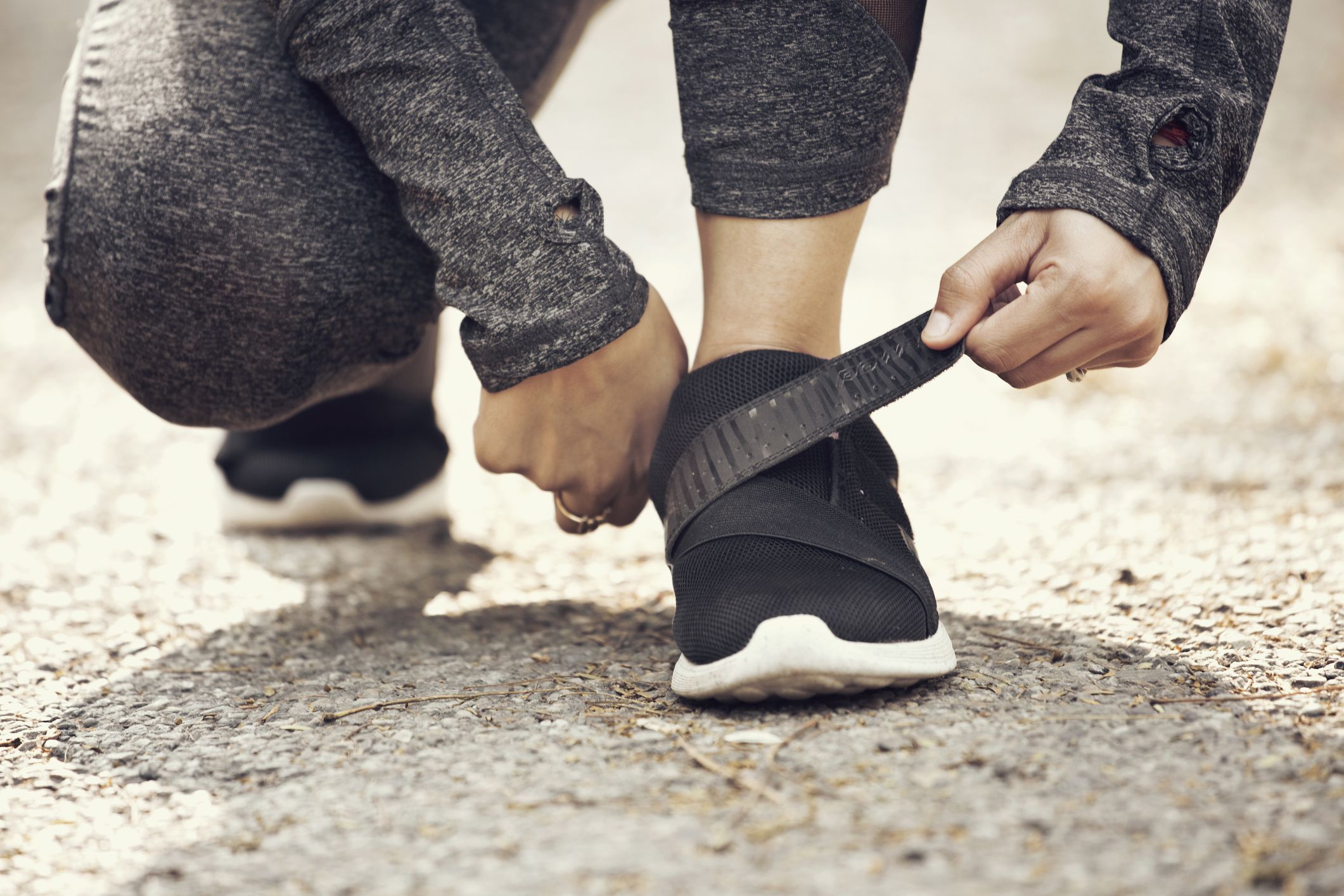 Low section of female runner fastening velcro closure of her sports shoe preparing for a jog.