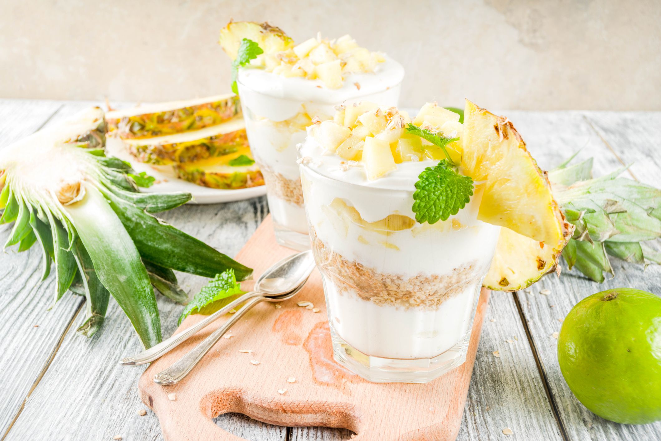 Pineapple breakfast layered parfait with Greek yogurt, homemade granola, pineapple slices, mint, wooden background,