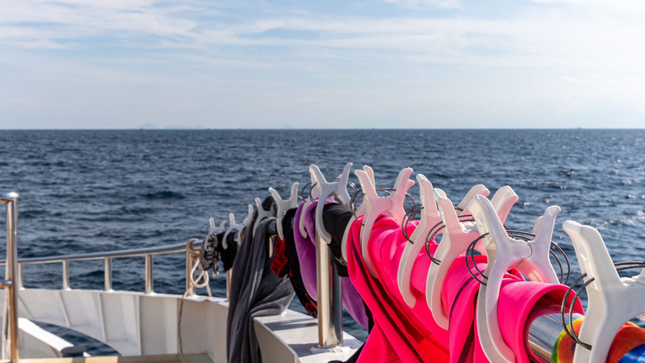 Closeup shot of towel hanging on an iron bar at a boat deck with white clippers and background of blue ocean and cloudy sky. Cloth drying on ship deck.