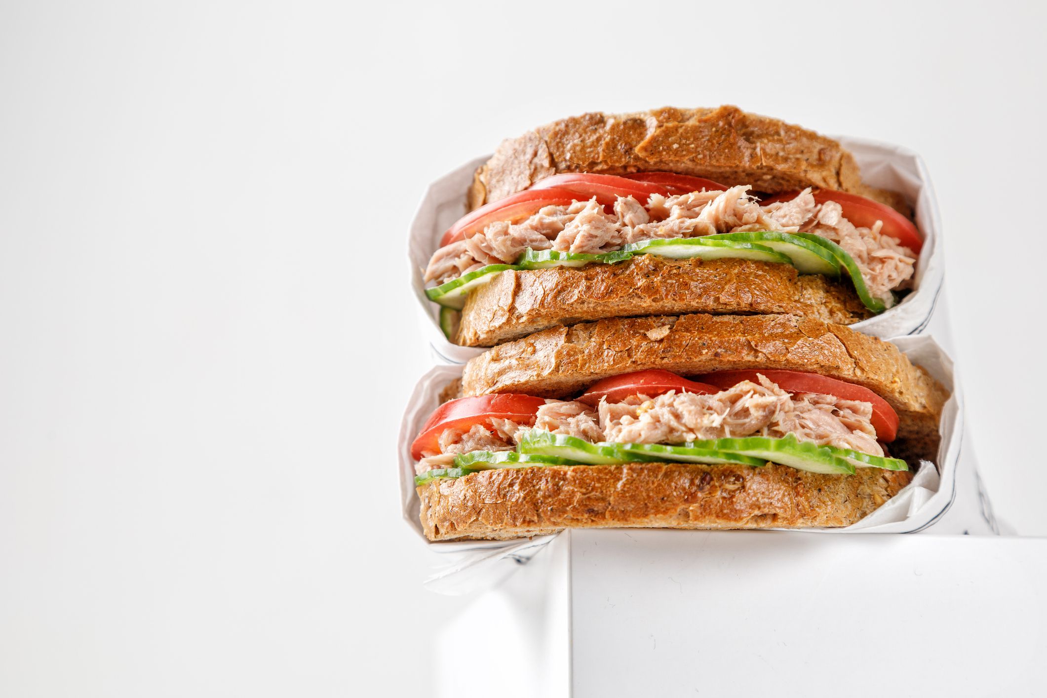 Two delicious tuna sandwiches with tomato and cucumber in paper on white box. low view point. Copy space.