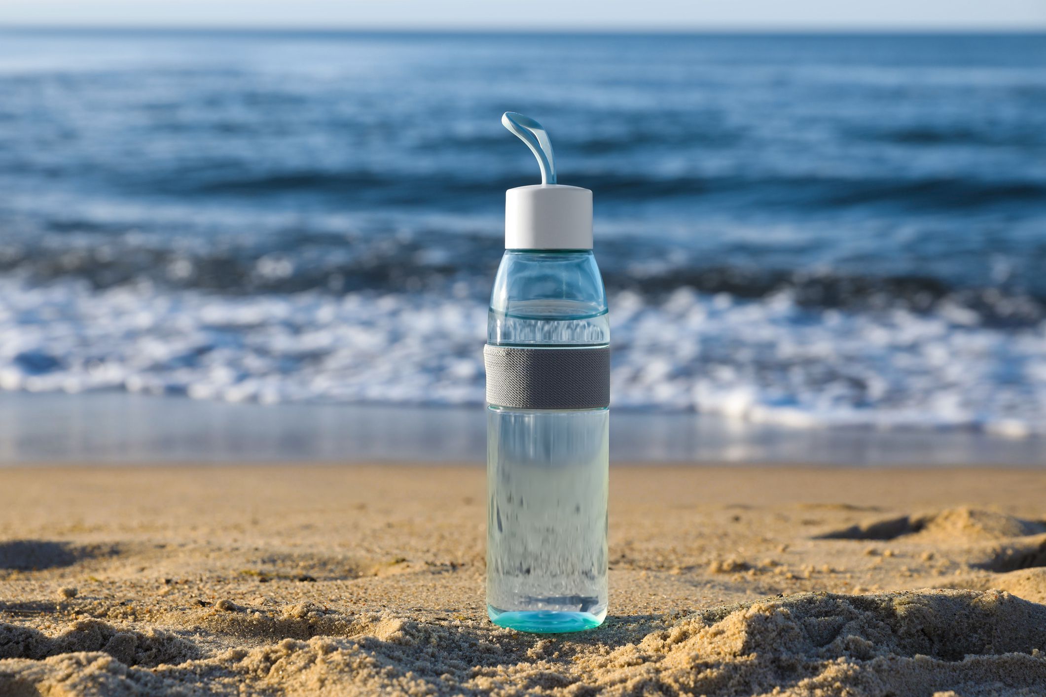 Glass bottle with water on wet sand near sea
