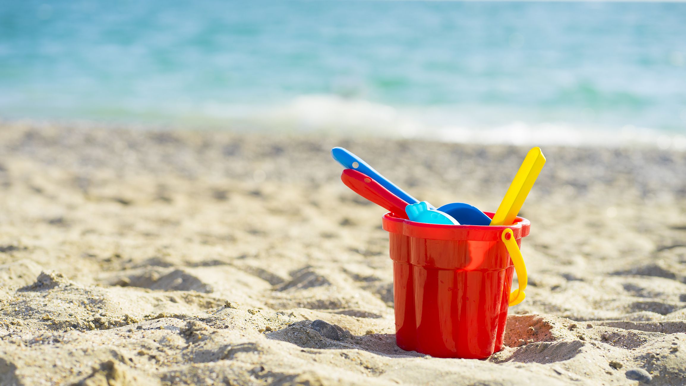 Red children's bucket with sand and toys on the seashore