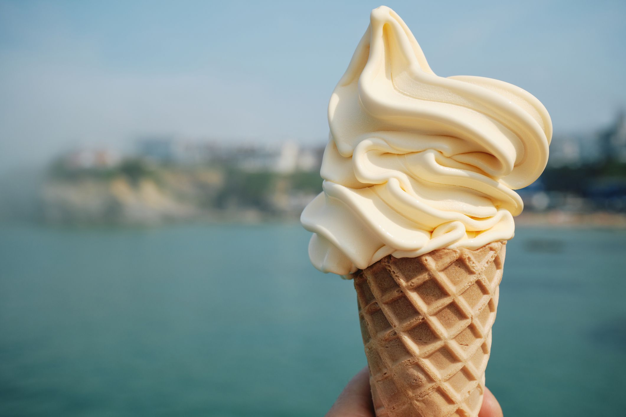 Hand holding an Ice Cream with Newquay town defocused in the background.