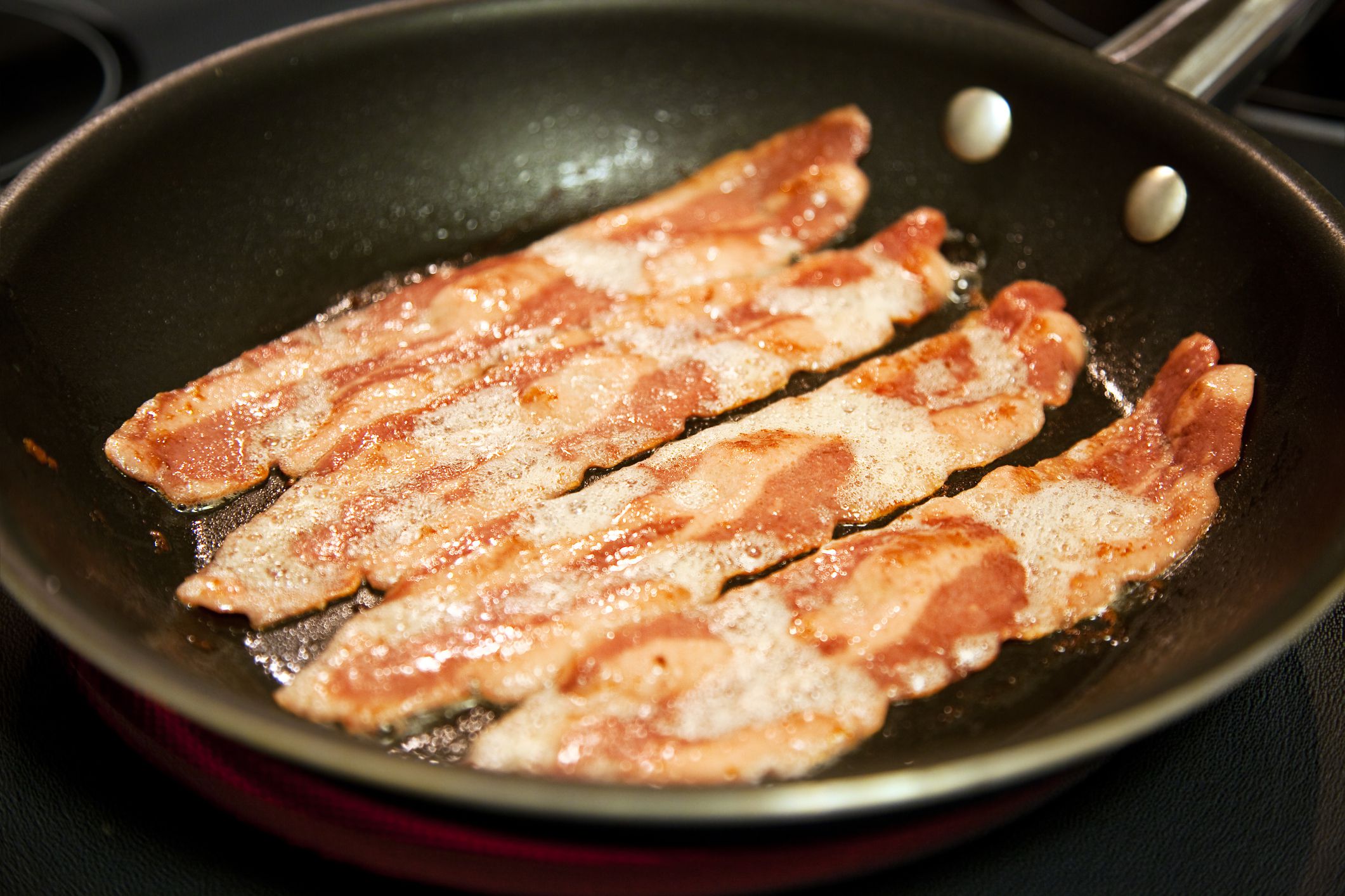 Cooking slices of healthy, low fat turkey bacon in a frying pan. Shallow depth of field.