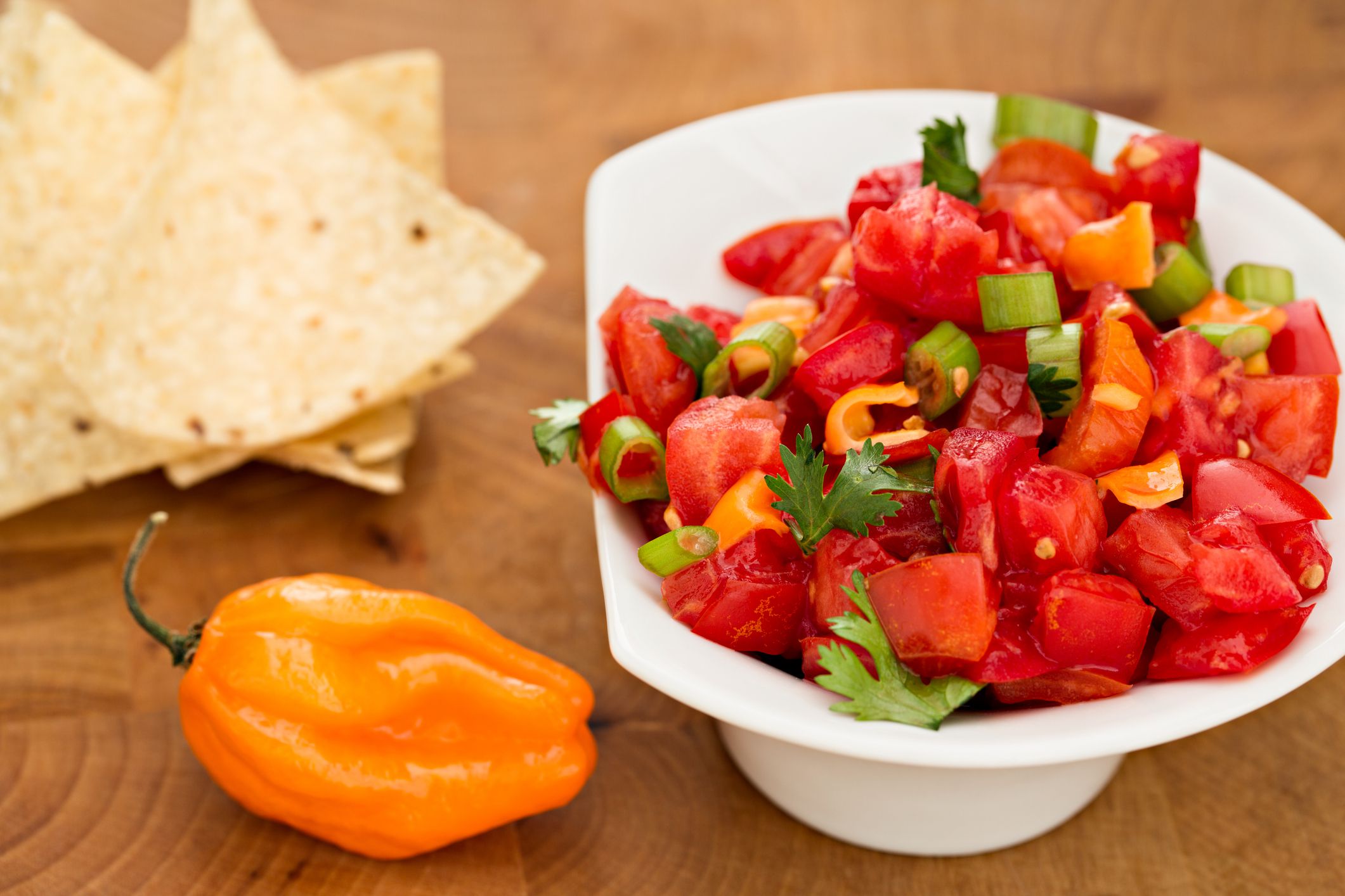 A high angle close up shot of a raw fresh picked habanero, spicy habanero salsa and chips.