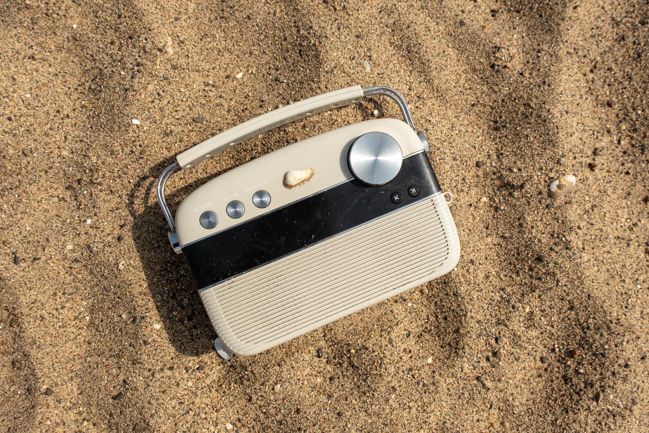 A vintage-style radio with an orange hue, perched atop a sandy beach shoreline, overlooking a tranquil ocean
