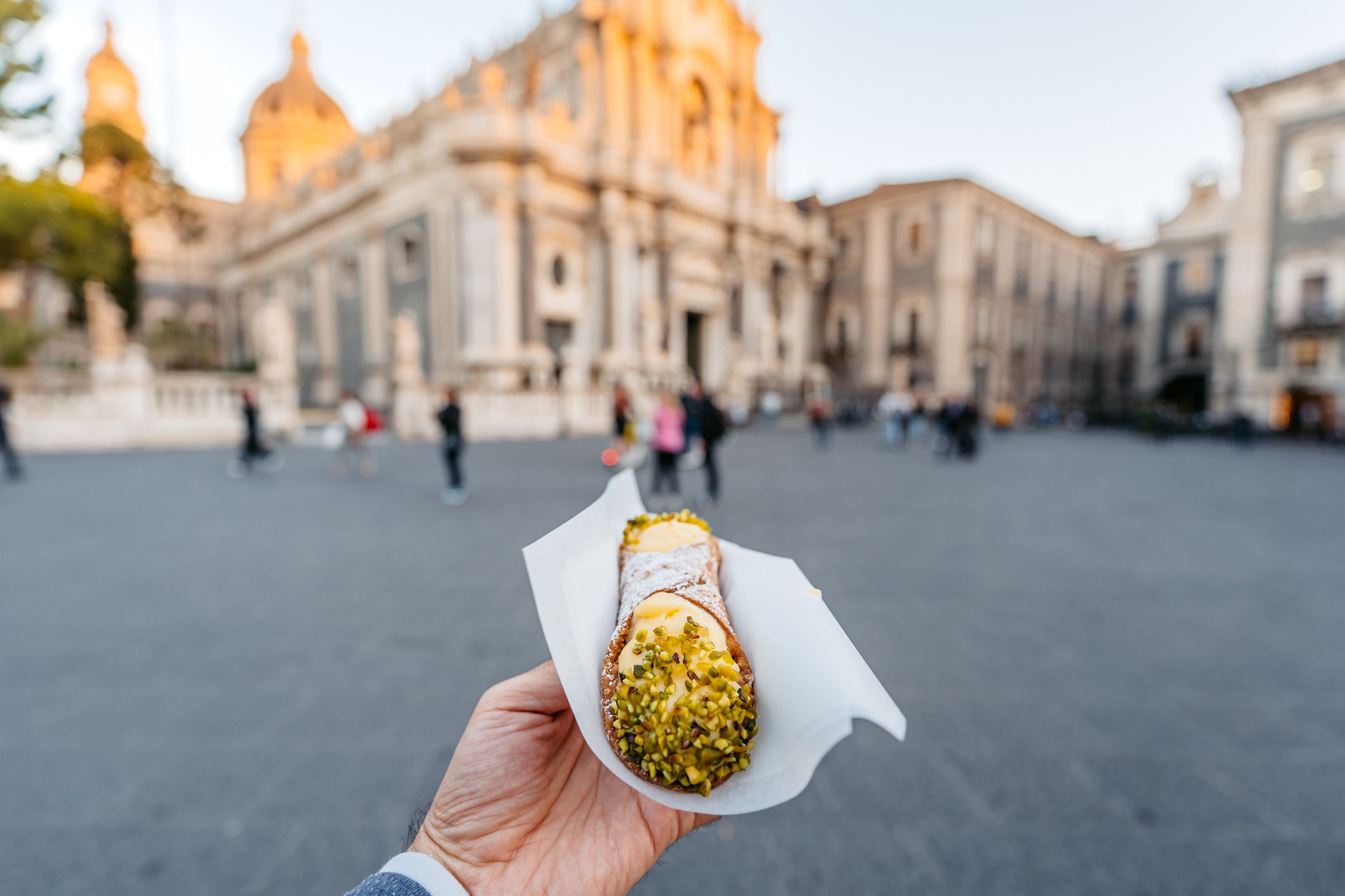 Young man holding a cannoli pastry filled with creamy ricotta and pistachios on the street in Catania, Sicily.